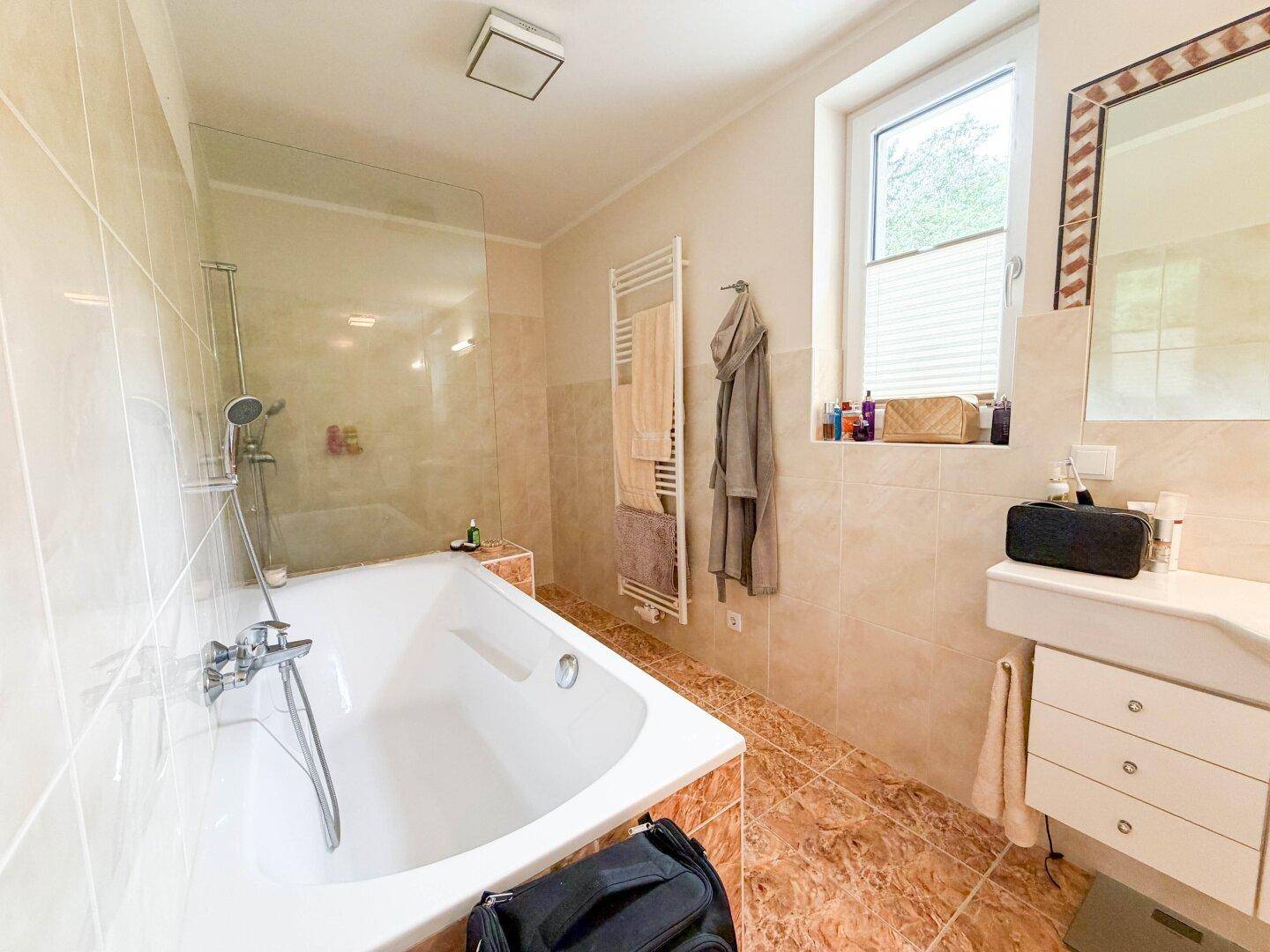 Modernes Badezimmer mit Badewanne, separater Dusche, Fenster und beheiztem Handtuchhalter.