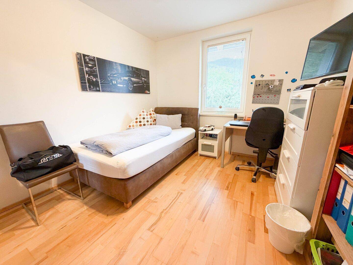 Helles Schlafzimmer mit Einzelbett, Schreibtisch und Holzfußboden, ideal als Kinder- oder Gästezimmer.