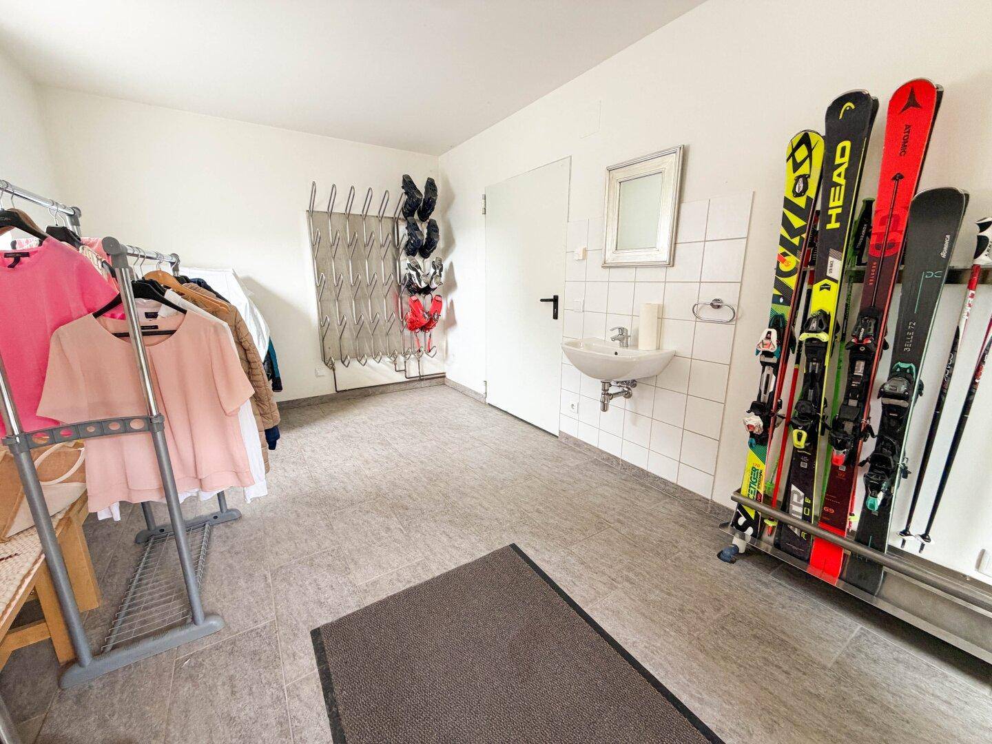 Praktischer Abstellraum mit Waschbecken, Skiständern und Kleiderstangen für Sportausrüstung.