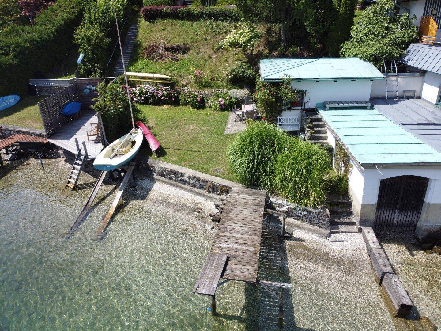 Luftaufnahme des Seegrundstücks mit mehreren Gebäuden, Garten, Steg und Booten am Ufer.