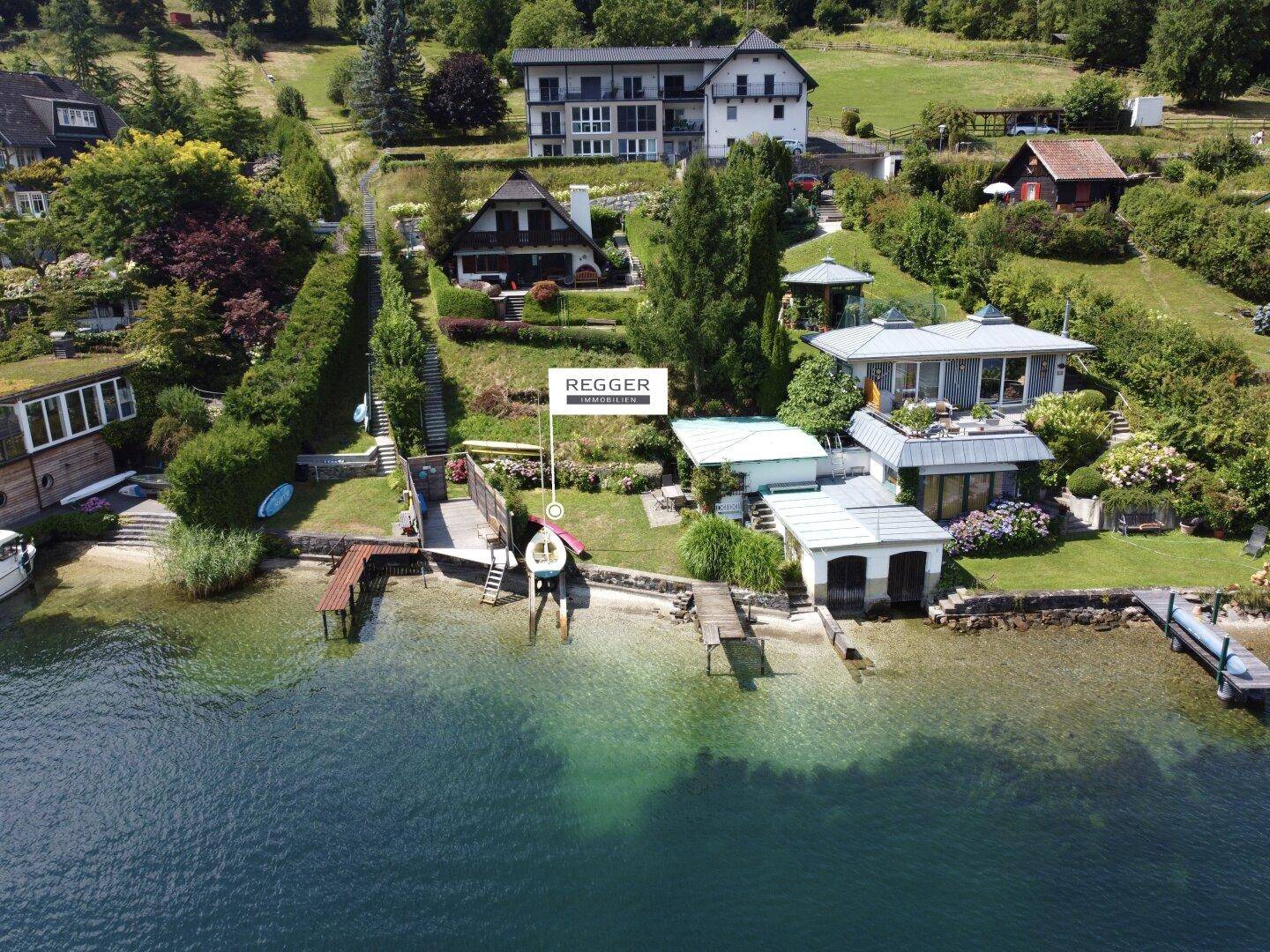 Gesamtansicht des Seegrundstücks mit mehreren Häusern, Stegen und der umliegenden Landschaft.