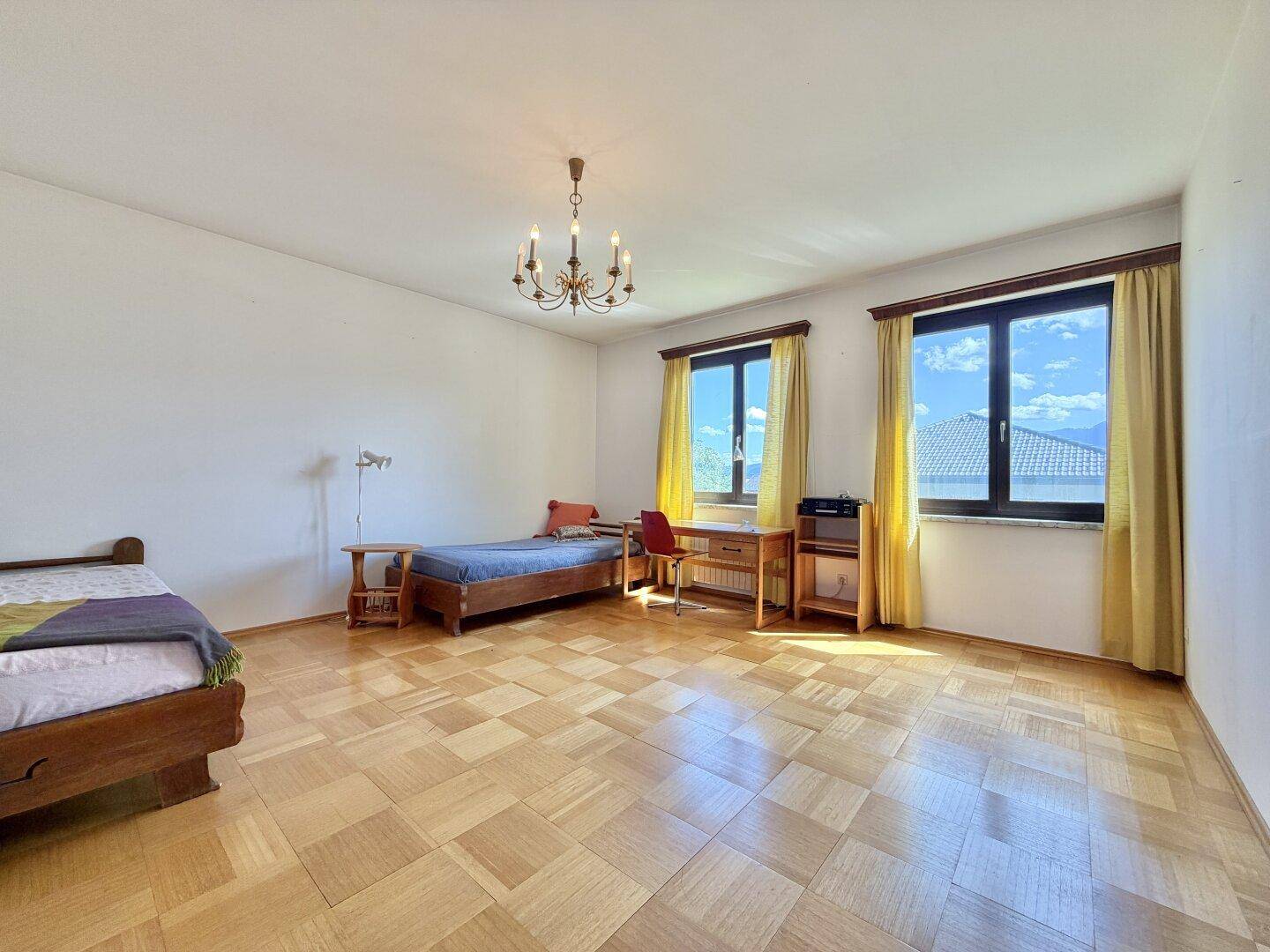 Helles Schlafzimmer mit zwei Einzelbetten, Holzboden und großen Fenstern.
