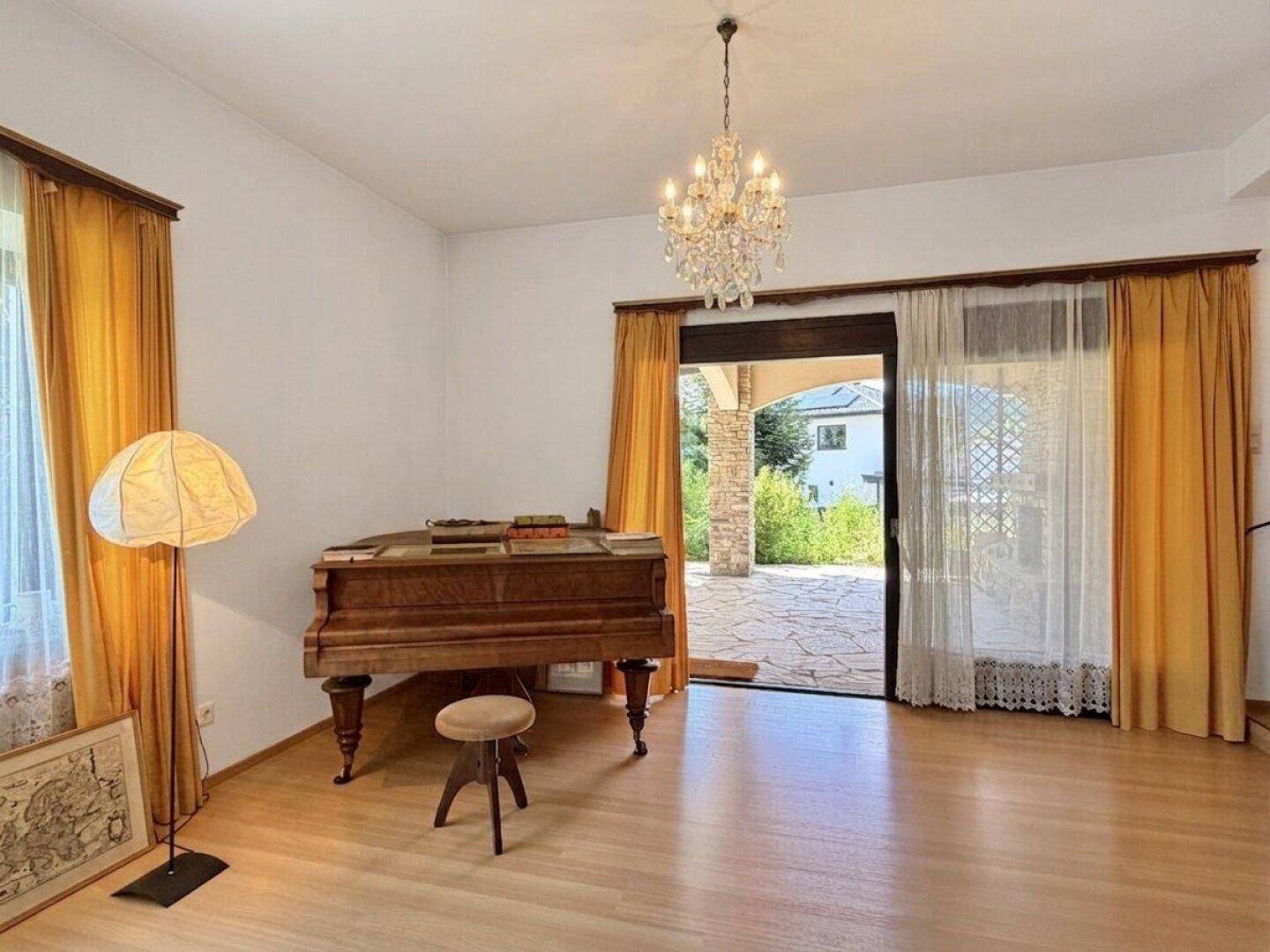 Helles Wohnzimmer mit Klavier, Kronleuchter und Zugang zur Terrasse.