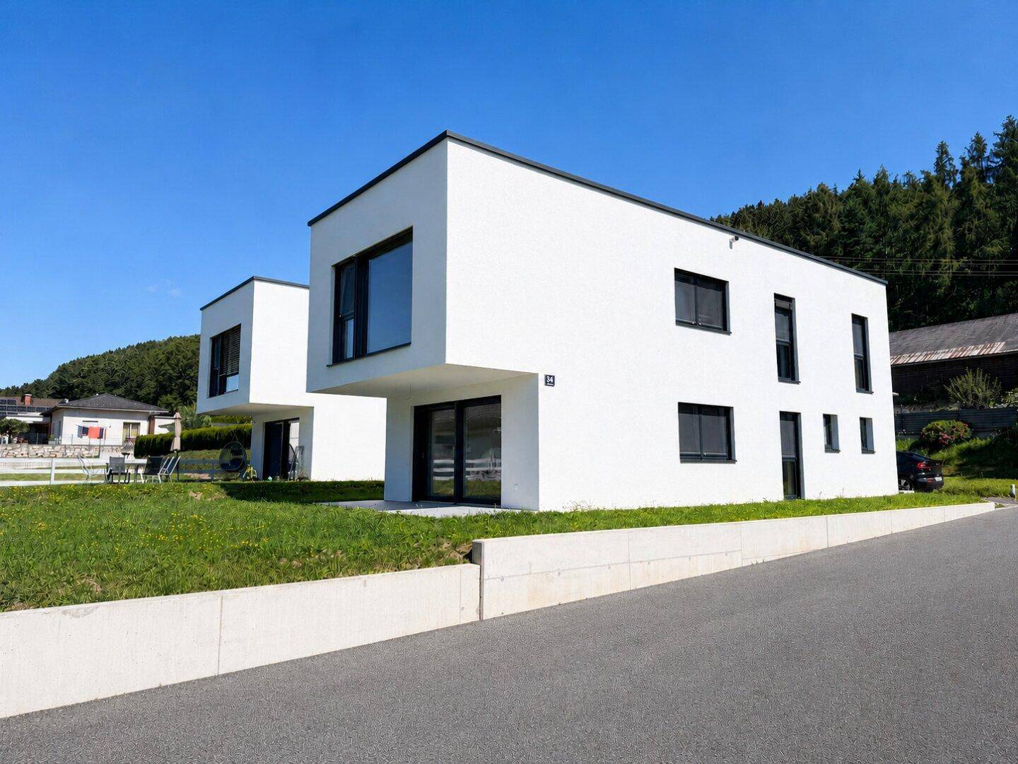 Zwei moderne Einfamilienhäuser mit weißer Fassade und Flachdach in einer ländlichen Umgebung.