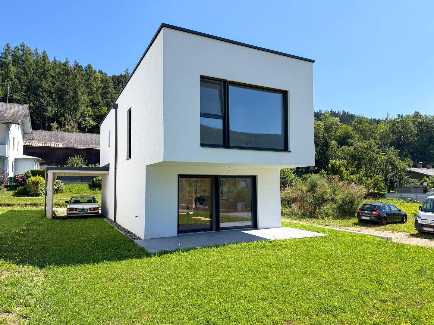 Modernes Einfamilienhaus mit weißer Fassade, großen Fenstern und Carport in sonniger Lage.