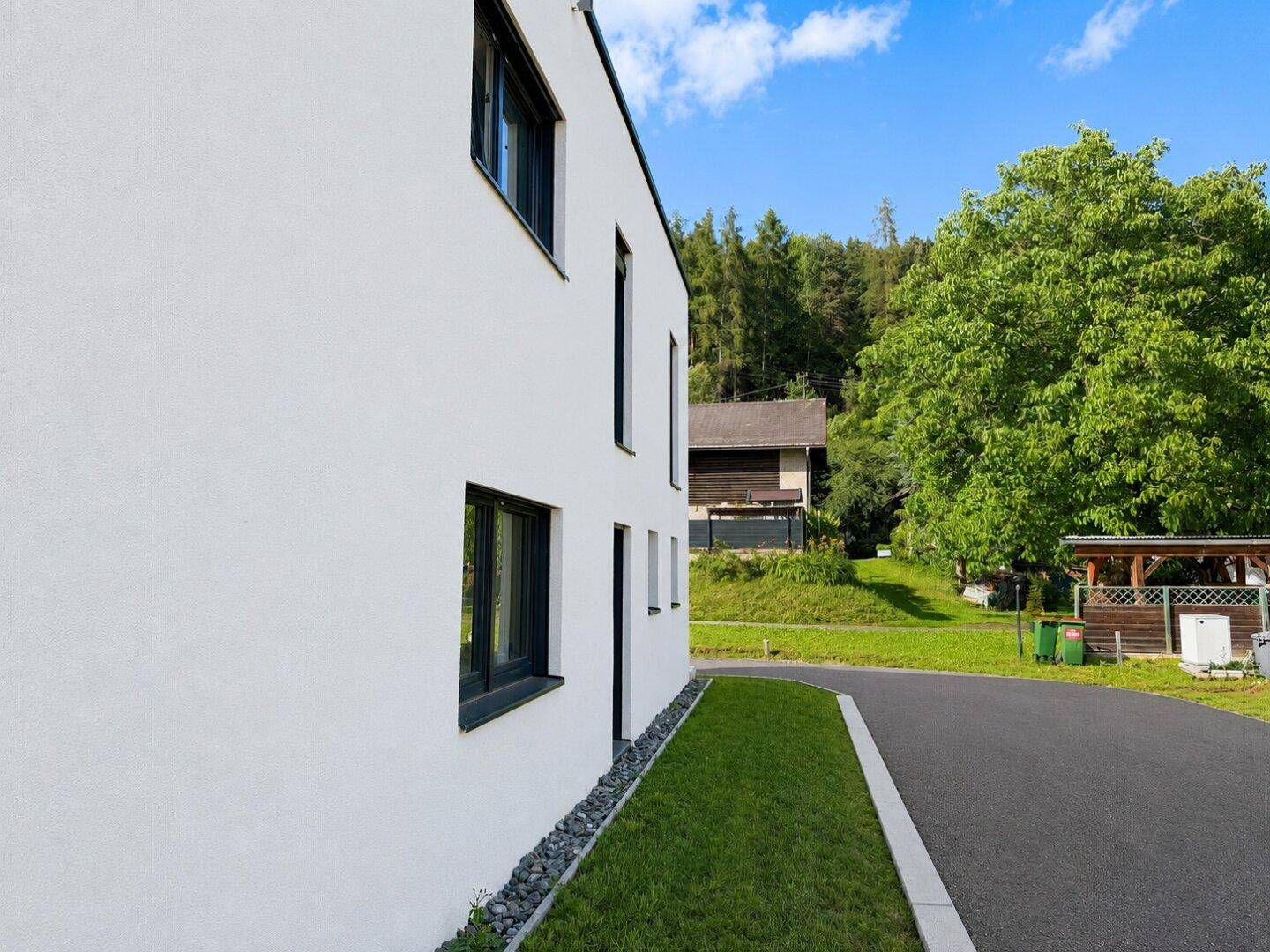 Seitenansicht des modernen Hauses mit Blick auf die grüne Umgebung und einen Wald im Hintergrund.