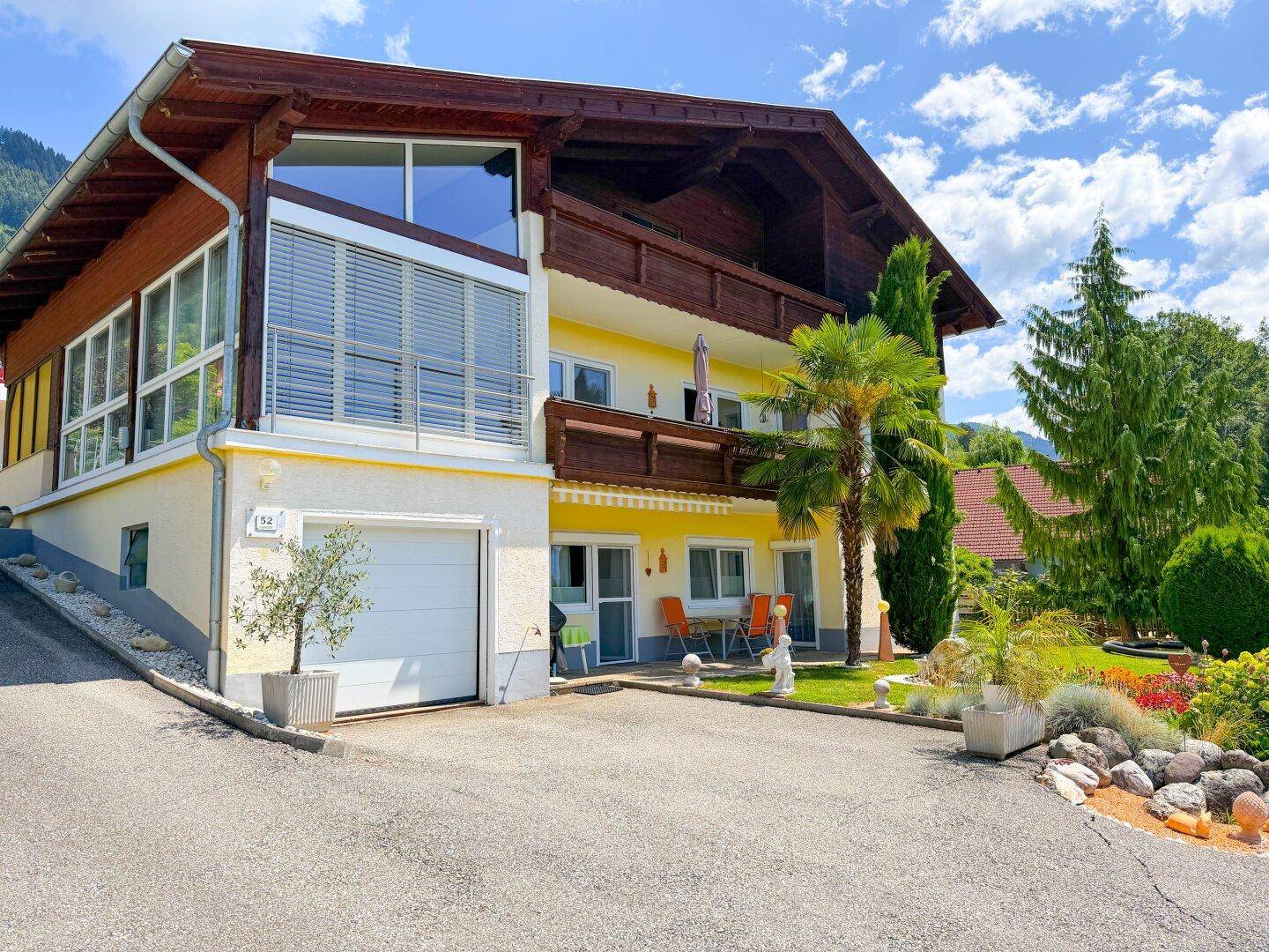 Vorderansicht des Hauses mit Garage, Garten und Balkonen.