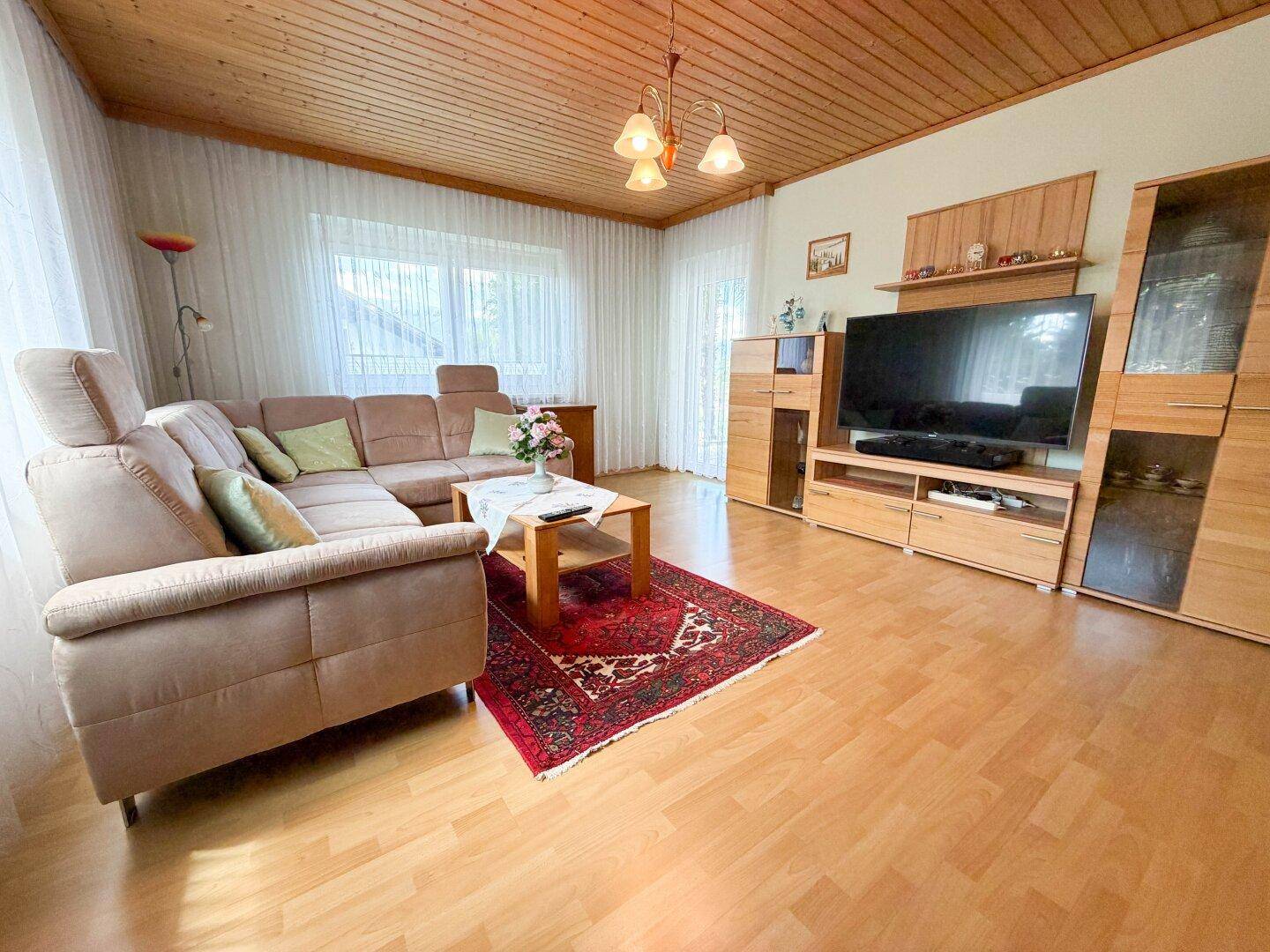 Gemütliches Wohnzimmer mit bequemer Couch, Holzbalkendecke und Laminatboden.