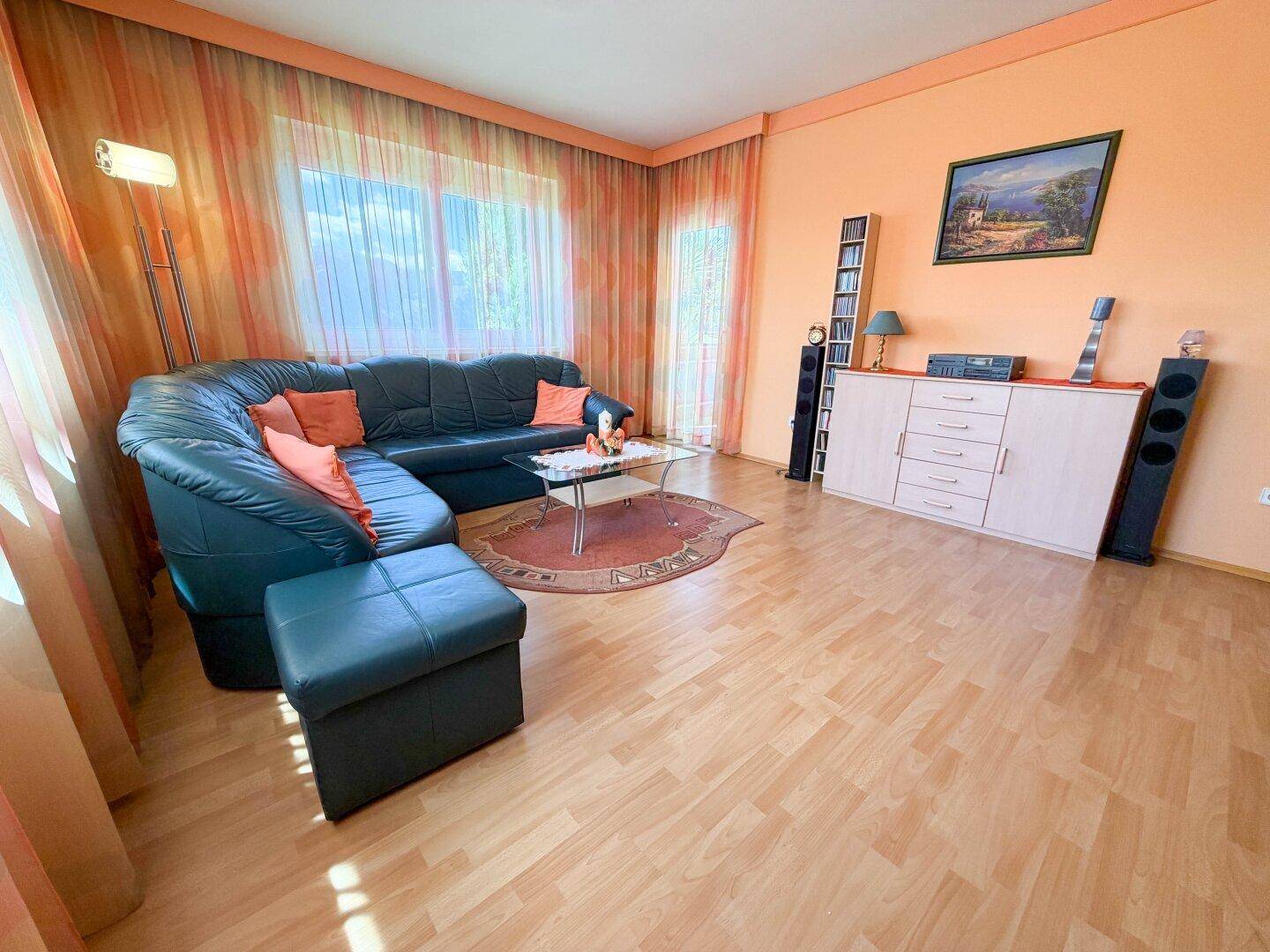 Geräumiges Wohnzimmer mit farbiger Wand, Ledersofa und Laminatboden.
