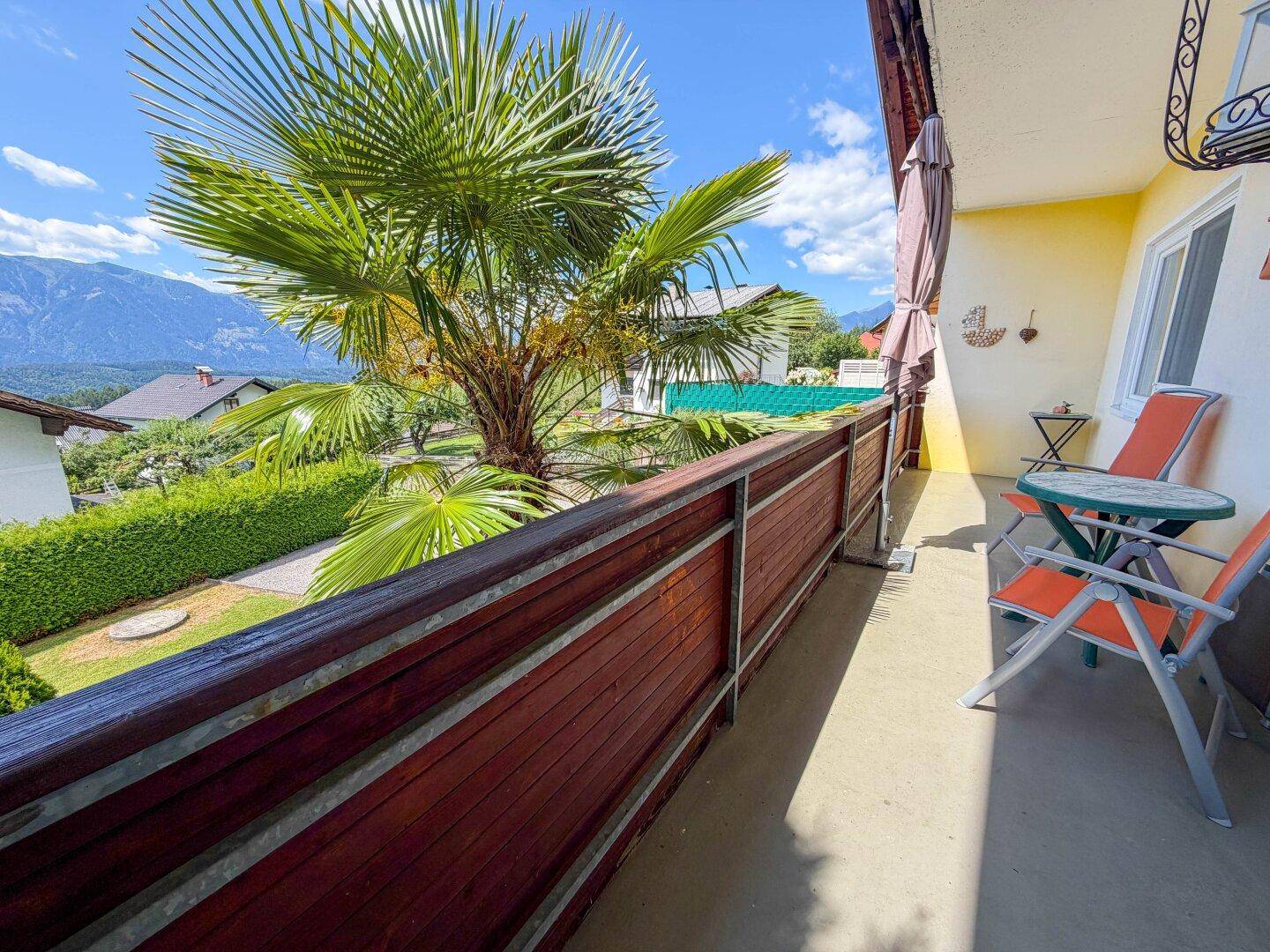 Sonnenverwöhnter Balkon mit Holzgeländer, Sitzgelegenheiten und Panoramablick auf die Berge.