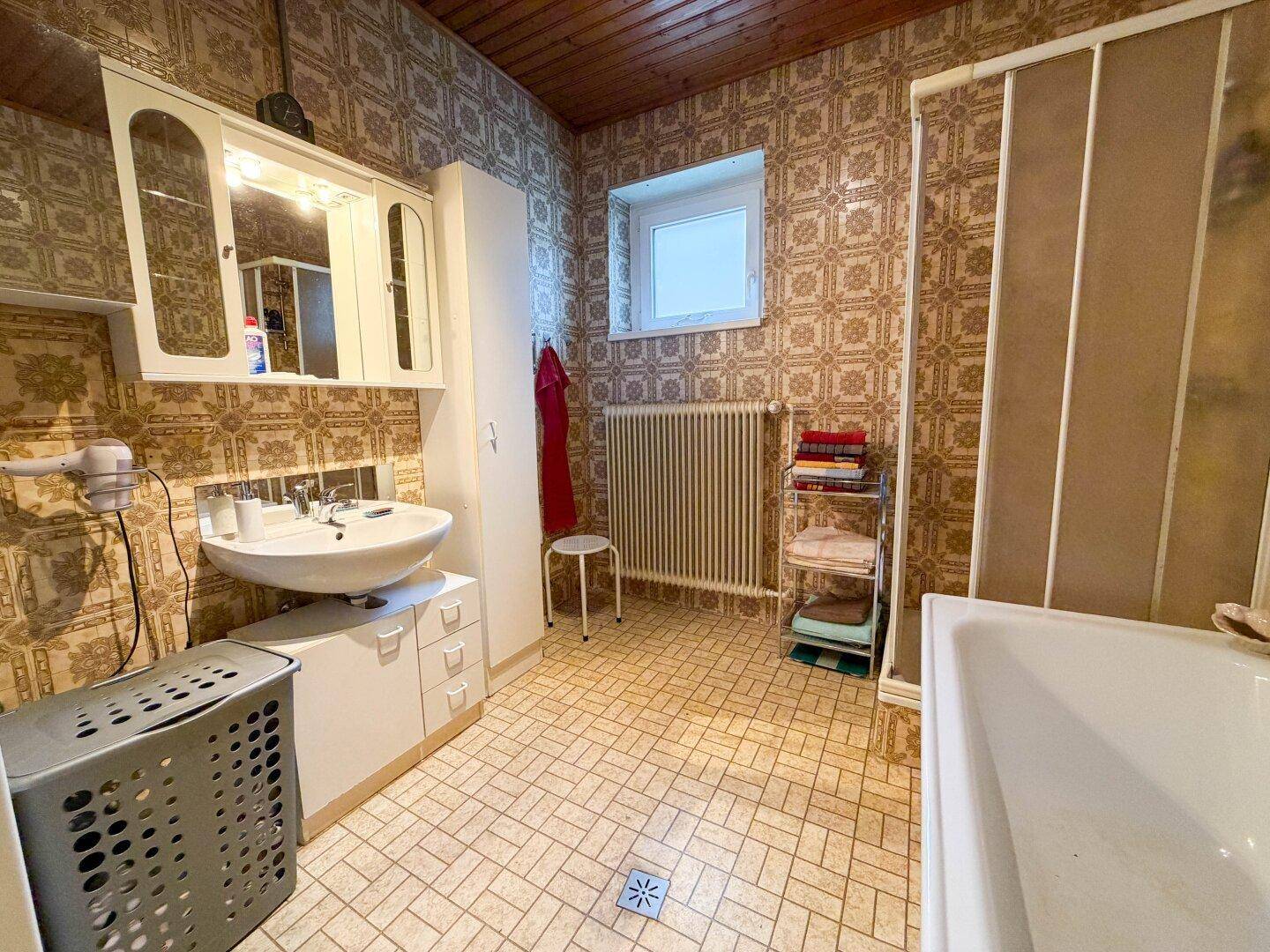 Badezimmer im 80er-Jahre-Stil mit gemusterten Fliesen, Badewanne und Holzdecke.