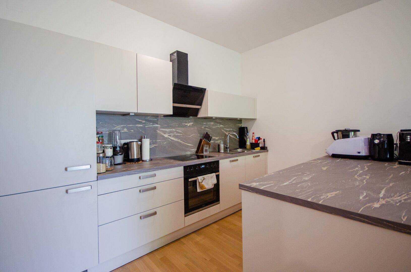 Moderne Einbauküche mit hellgrauen Fronten, dunkler Arbeitsplatte und integrierten Geräten.