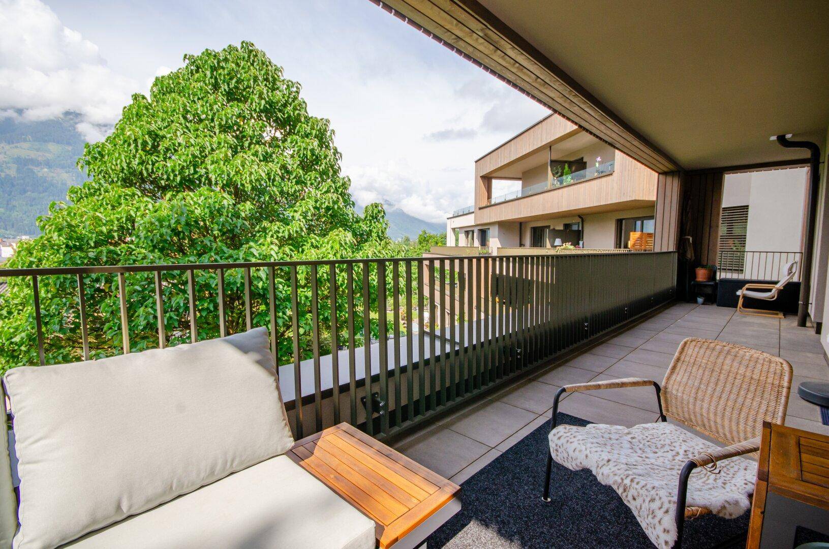 Breiter Balkon mit bequemen Sitzmöbeln und üppigem Grünblick auf Bäume und Berge.