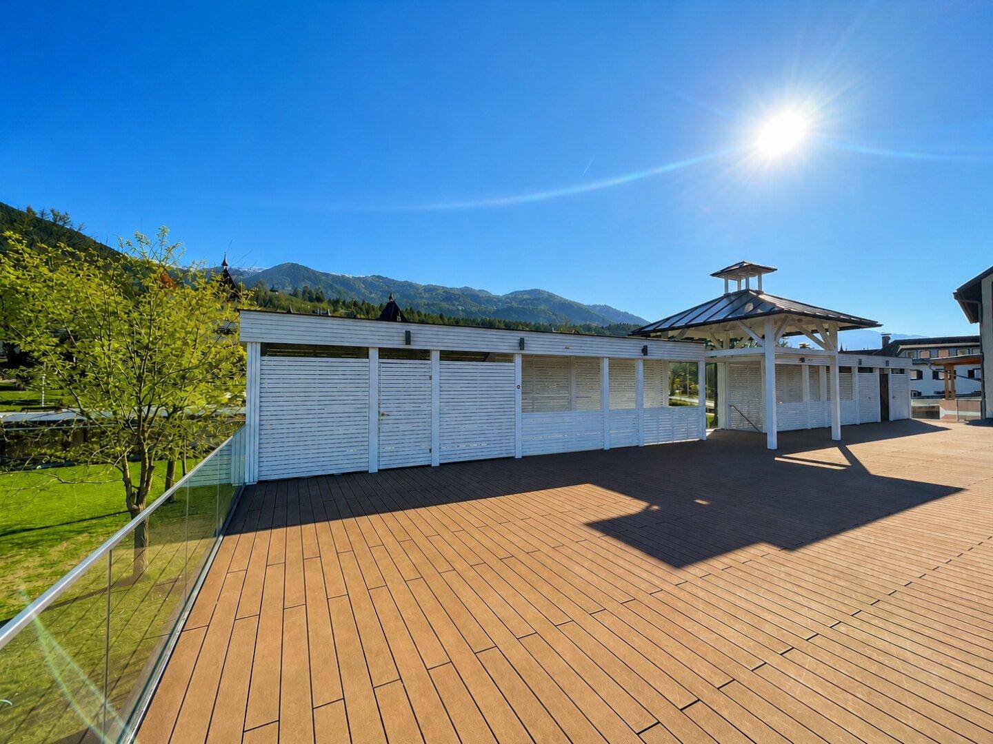 Große Holzterrasse mit weißem Pavillon und Blick auf grüne Wiesen und die umliegenden Berge.