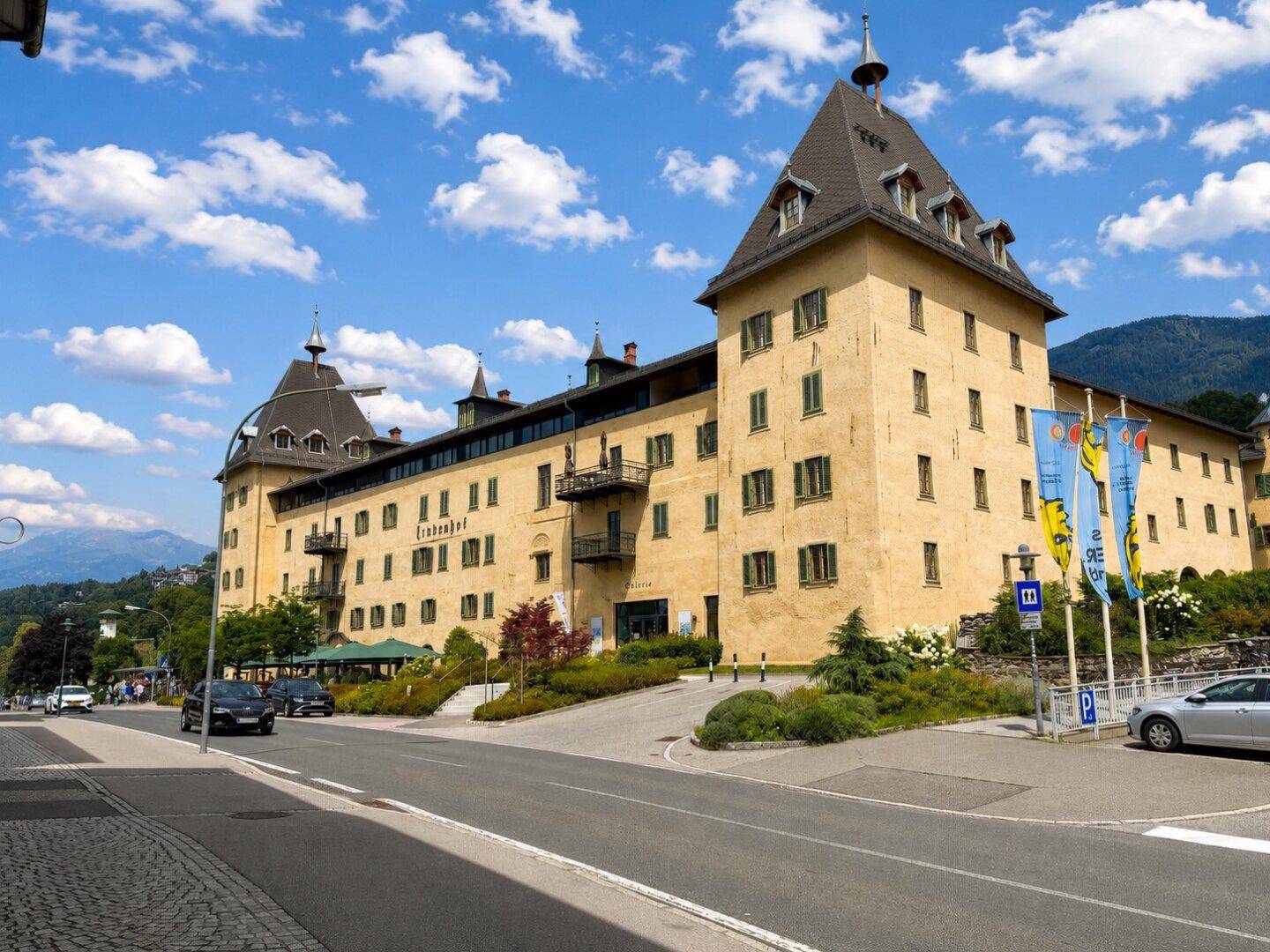 Historisches gelbes Gebäude mit markanten Dächern und vielen Fenstern, gelegen an einer Straße mit Bergen im Hintergrund.