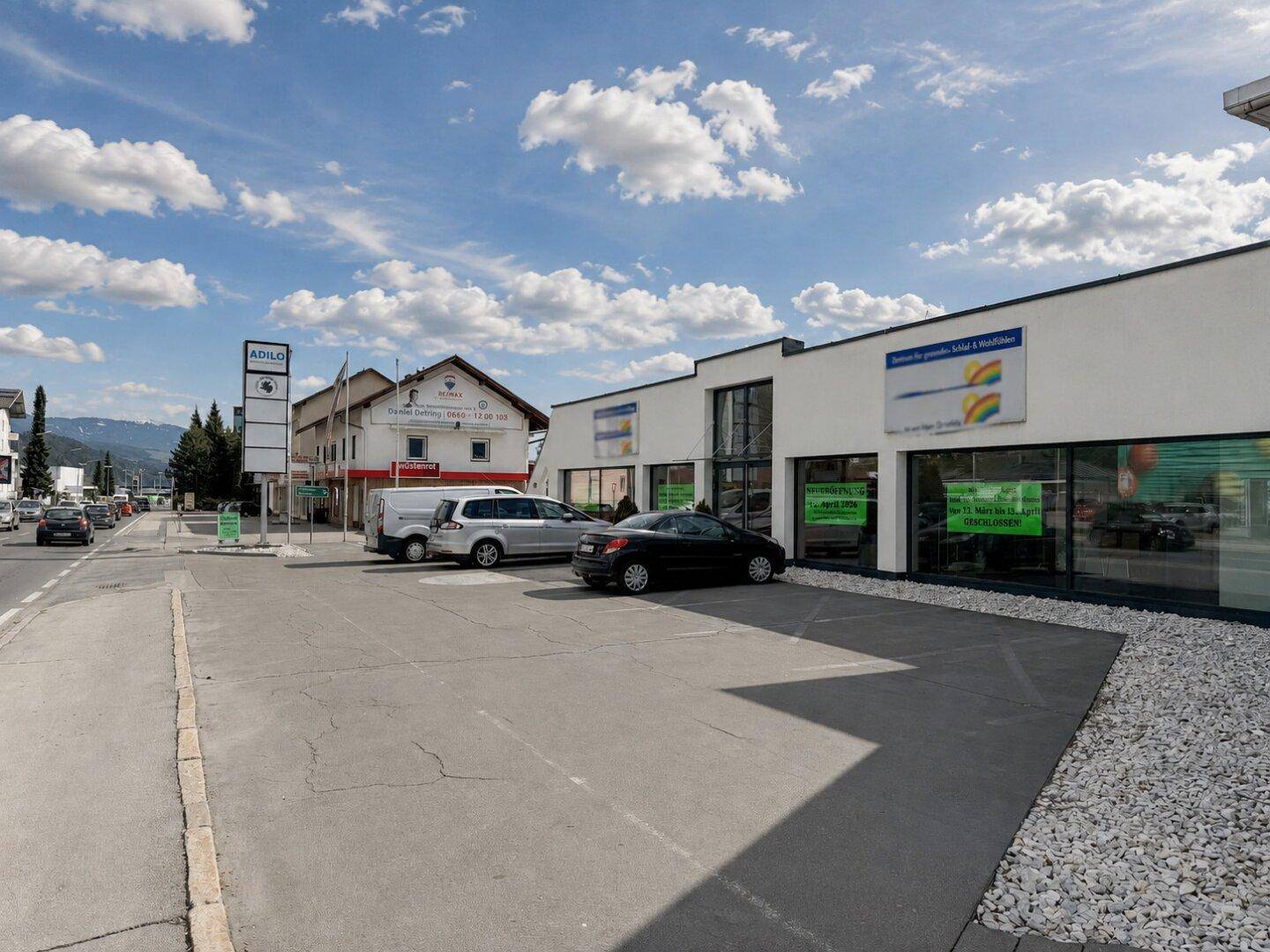 Ansicht des Gewerbegebäudes von der Straße aus mit Parkmöglichkeiten und klarem Himmel.