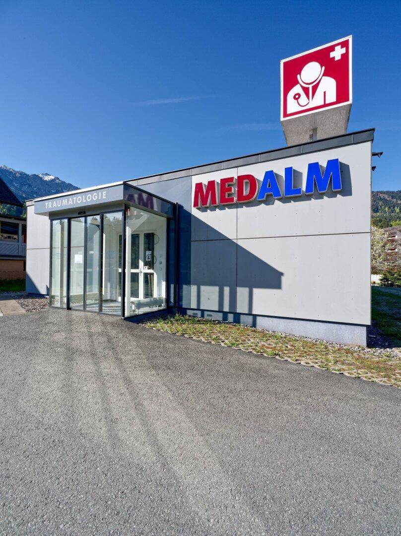 Moderne Außenansicht des medizinischen Gebäudes mit Glasportal und dem Schriftzug "Traumatologie".