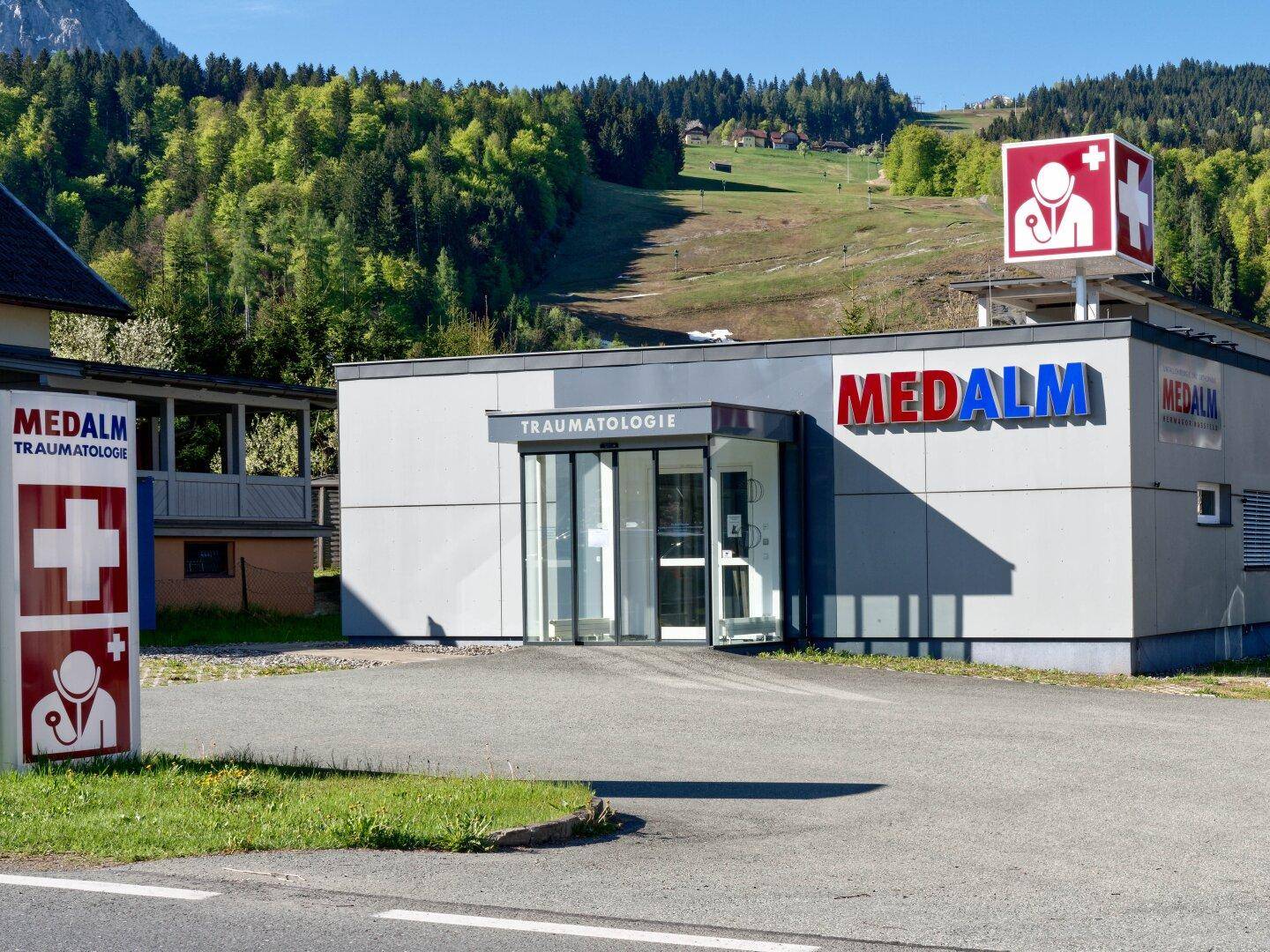 Außenansicht eines medizinischen Gebäudes mit Beschilderung und einem Hügel im Hintergrund.