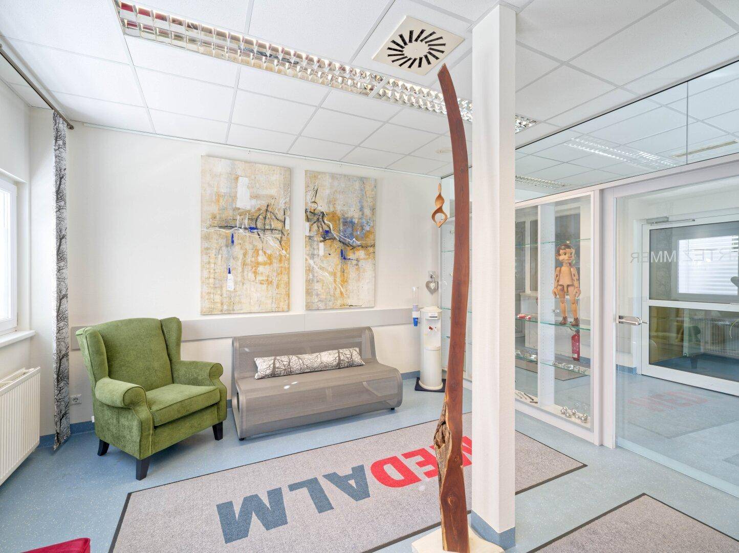 Helle Wartezone mit bequemen Sitzgelegenheiten, Kunstwerken an der Wand und einem Teppich mit Logo.