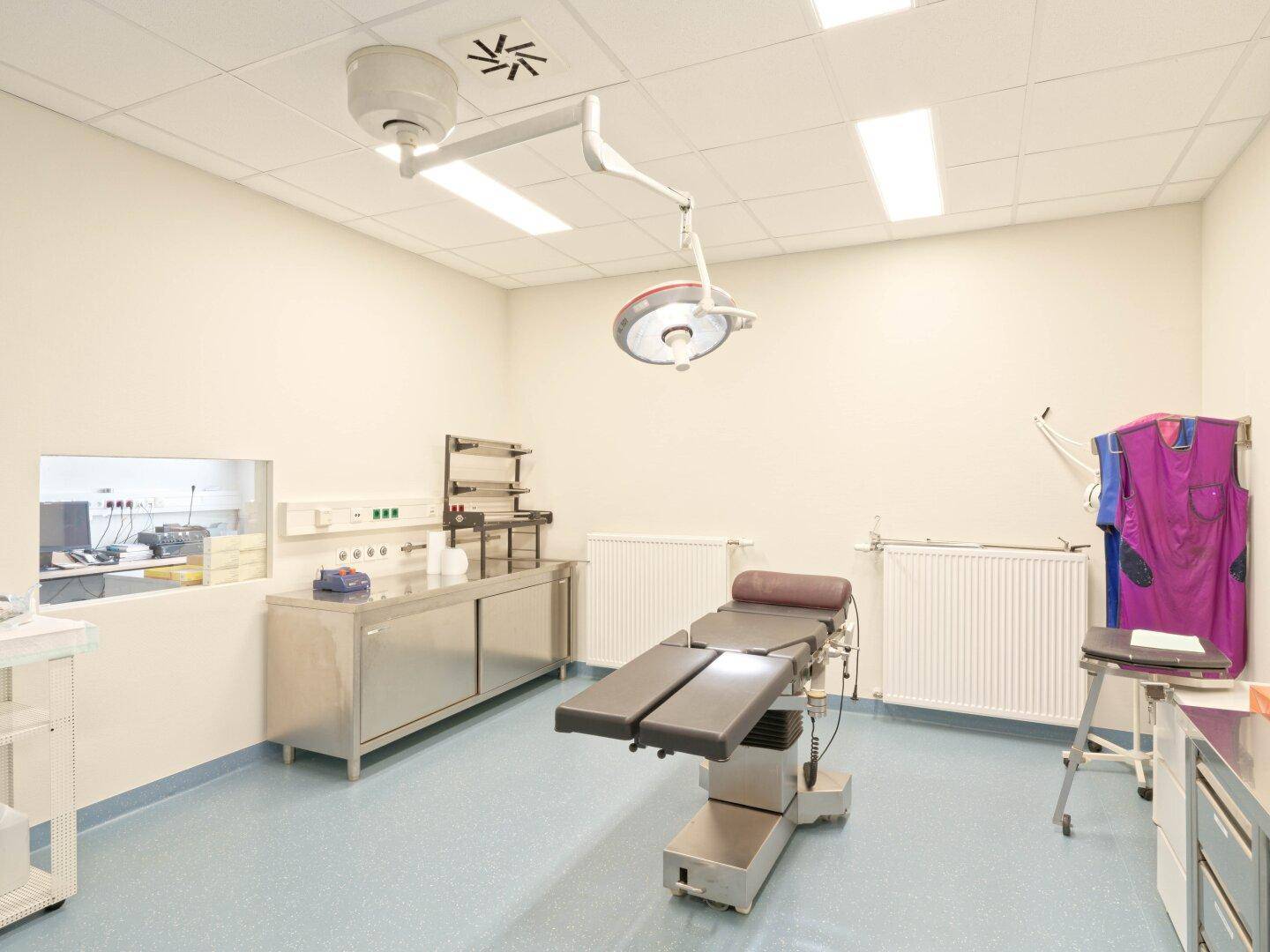 Behandlungsraum mit Untersuchungsliege, medizinischen Geräten und einem Operationslicht an der Decke.