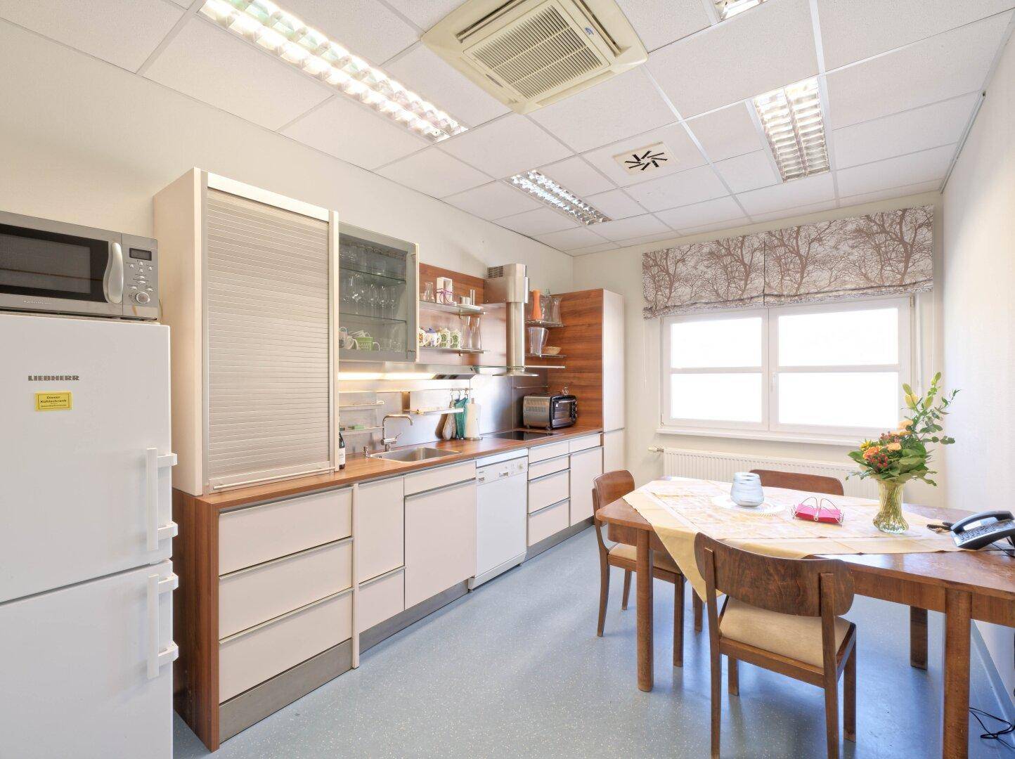 Funktionale Küchenzeile mit Esstisch, Kühlschrank und Mikrowelle, ideal für Personal.