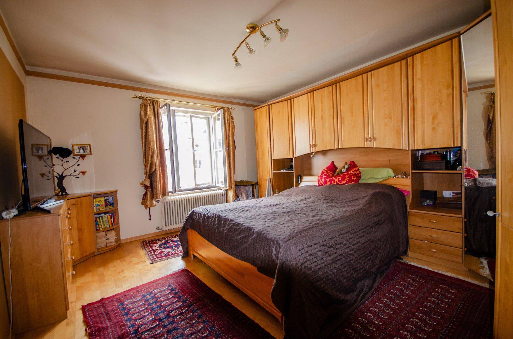 Schlafzimmer mit großem Bett, Einbauschränken aus Holz und einem Fenster.