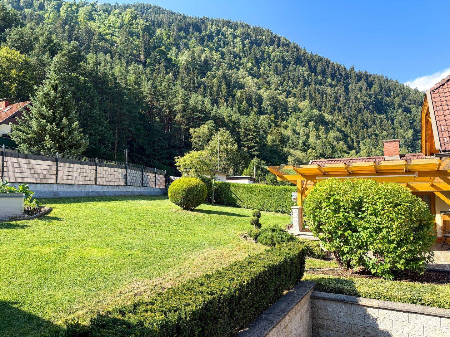 Weitläufiger Garten mit gepflegtem Rasen, Formschnitthecken und beeindruckendem Bergblick.