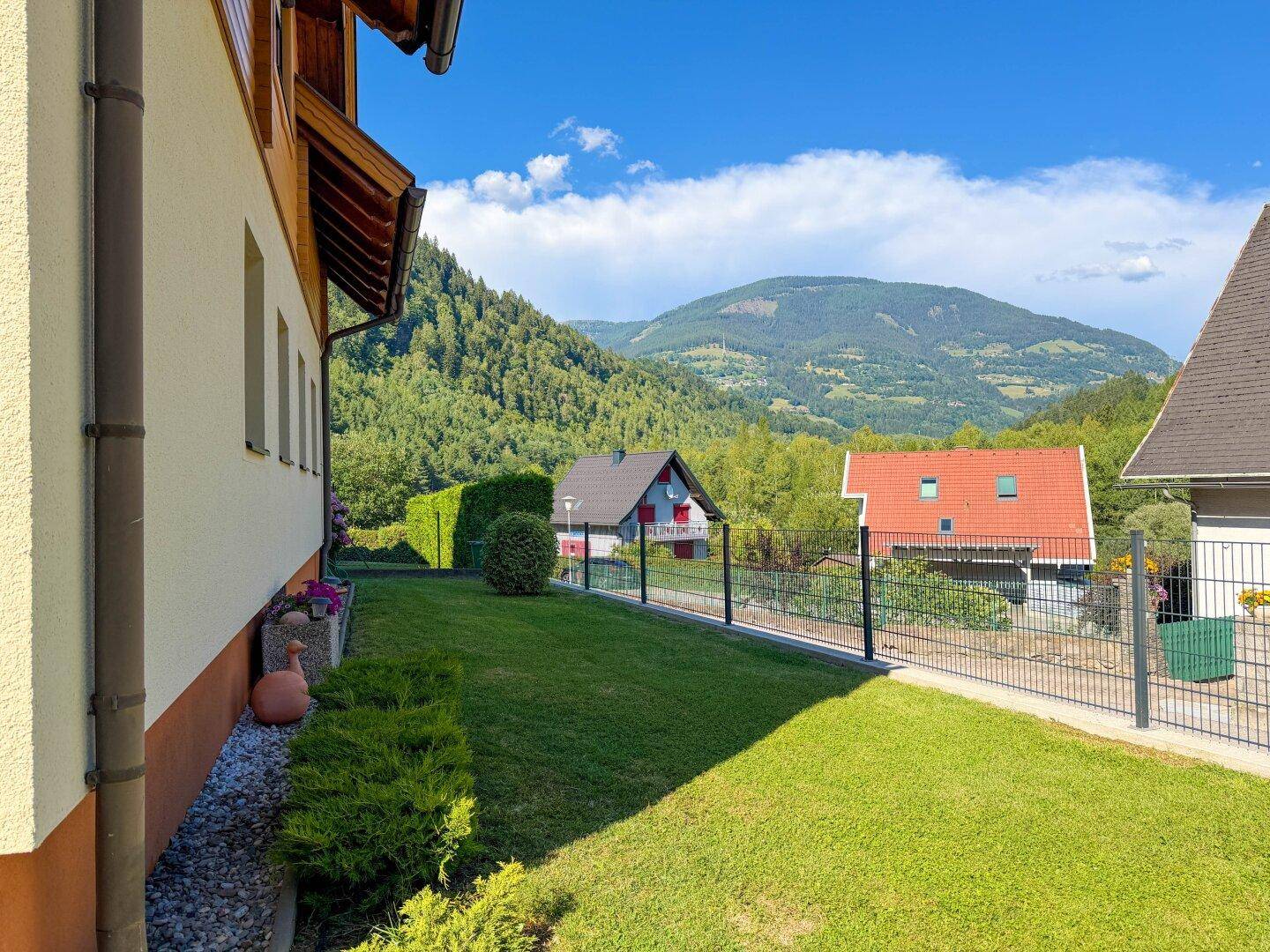 Seitlicher Gartenbereich mit Rasenfläche und weitem Blick auf die umliegende Berglandschaft.