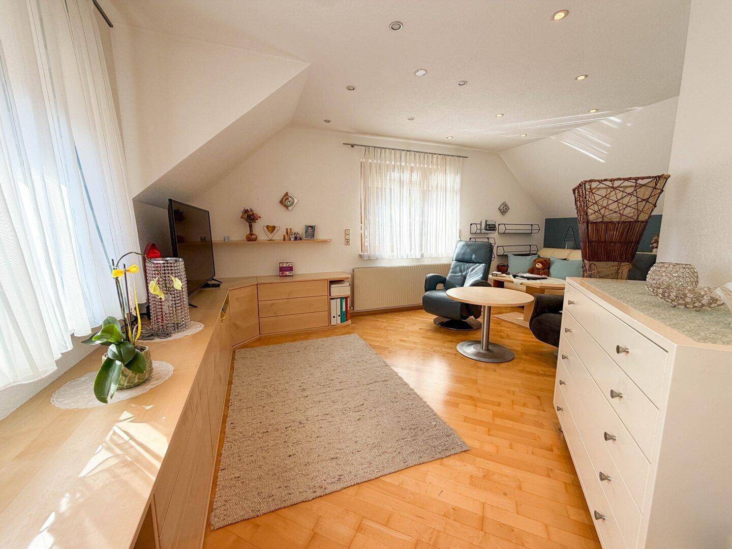 Helles Wohnzimmer im Dachgeschoss mit Holzboden, Dachschrägen und gemütlicher Einrichtung.