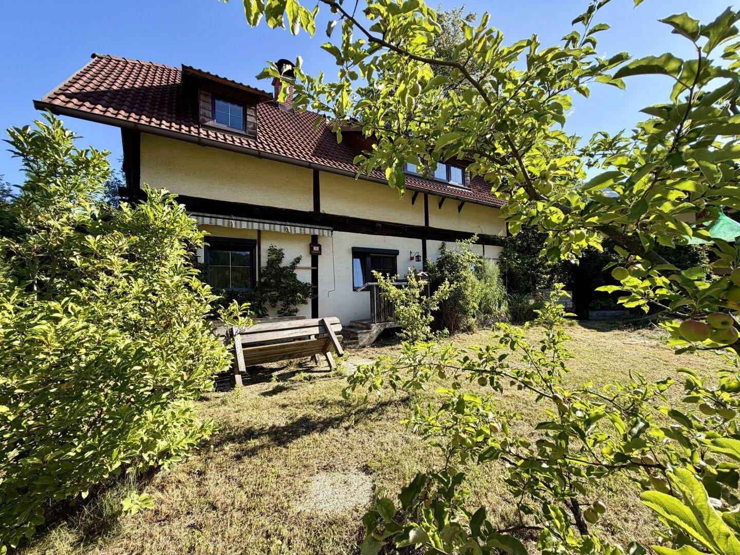 Vorderansicht des Hauses mit traditioneller Architektur, umgeben von einem grünen Garten und Obstbäumen.