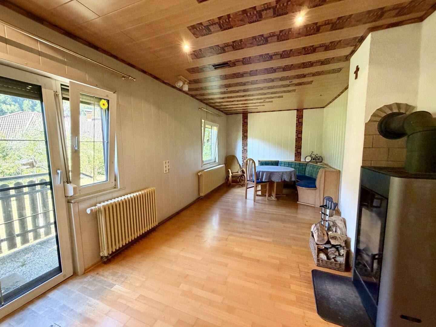 Helles Wohnzimmer mit Holzboden, Kaminofen und Zugang zu einem Balkon mit Bergblick.