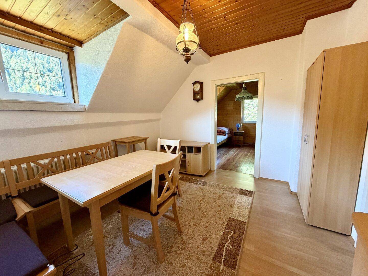 Gemütlicher Essbereich im Dachgeschoss mit Holztisch, Bänken und Zugang zu einem weiteren Zimmer.