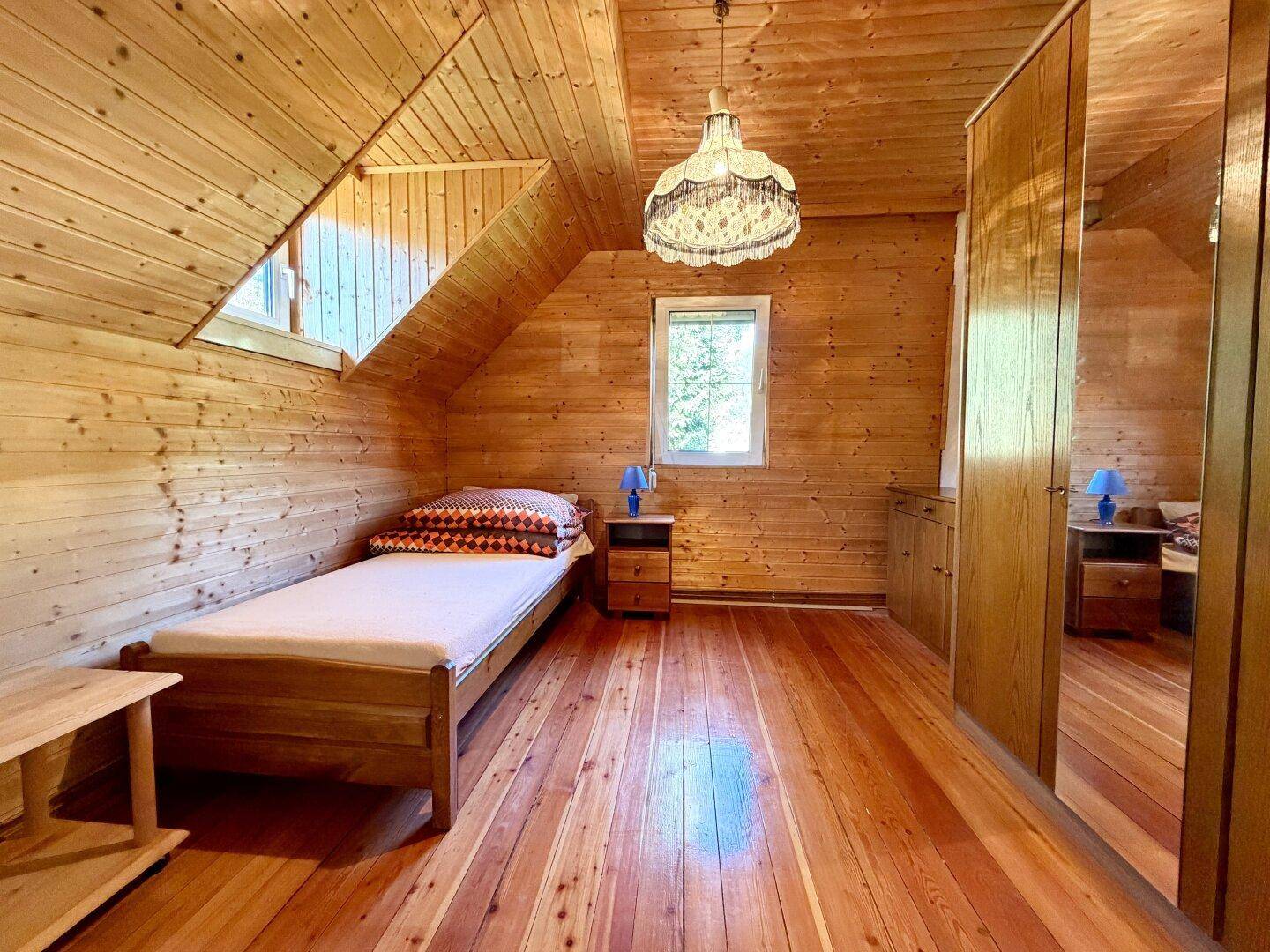 Rustikales Schlafzimmer im Dachgeschoss mit Holzboden, Holzverkleidung und Einzelbett.