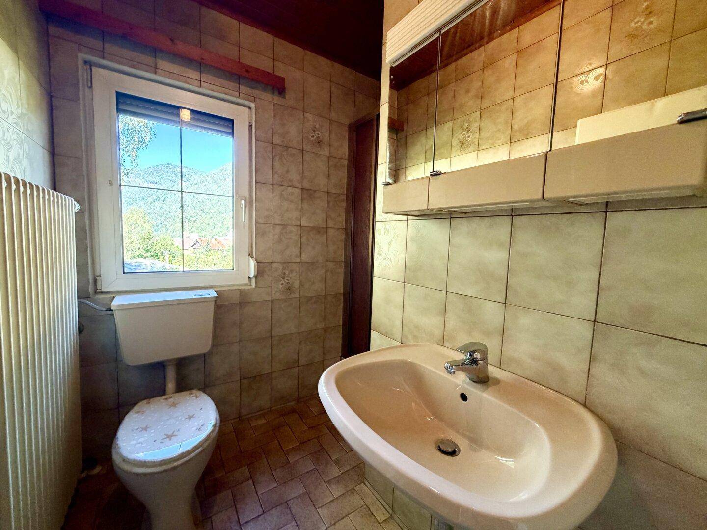 Kleines Badezimmer mit WC, Waschbecken und Fenster, ausgestattet mit hellen Fliesen.
