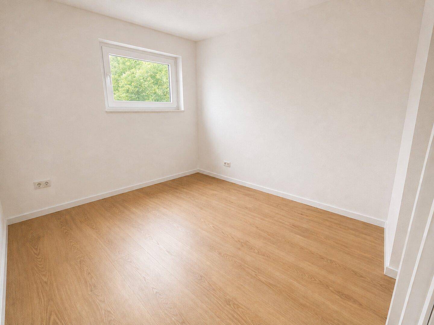 Helles Schlafzimmer mit Laminatboden, weißen Wänden und Blick ins Grüne durch das Fenster.