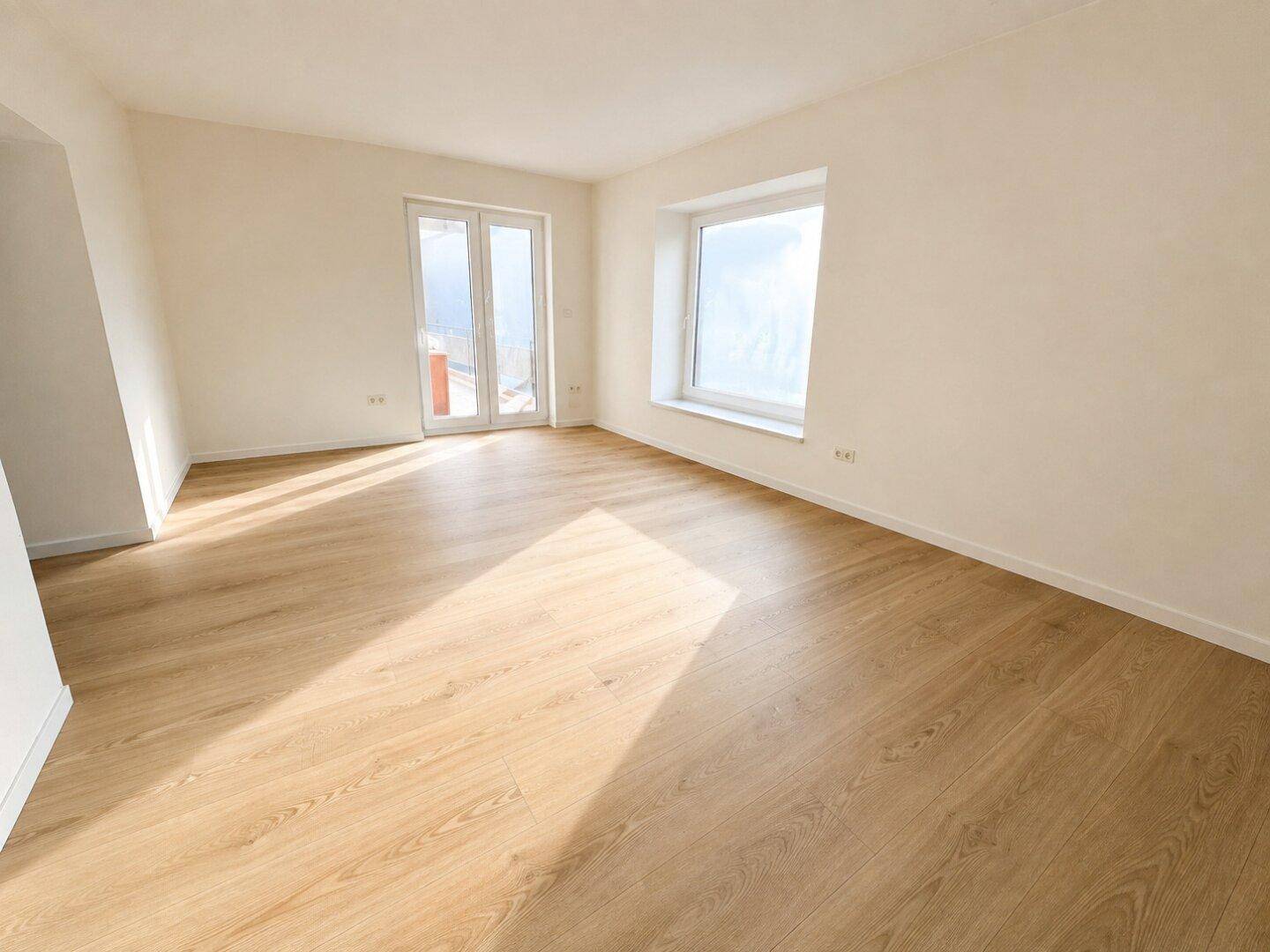 Heller Wohnraum mit neuem Laminatboden, weißen Wänden und Zugang zu einem Balkon.