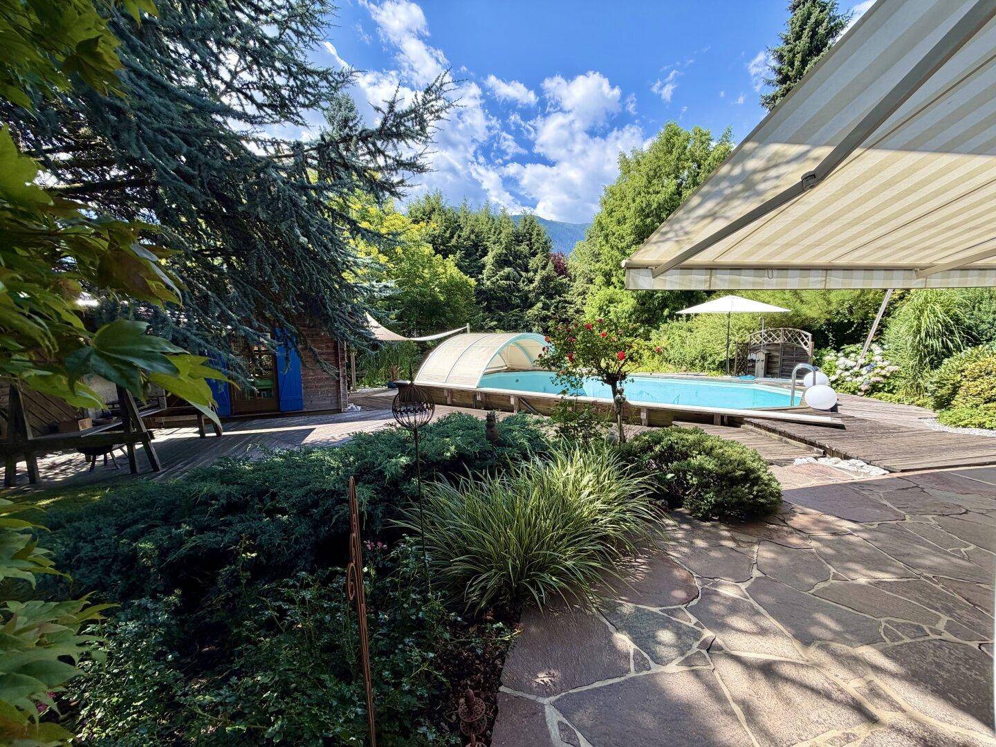 Entspannender Gartenbereich mit Pool, Steinplattenweg und schattenspendenden Bäumen an einem sonnigen Tag.