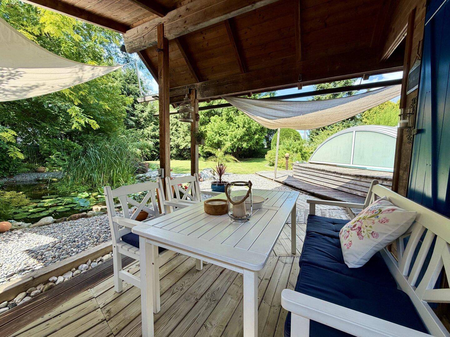 Gemütlicher überdachter Terrassenbereich mit Esstisch und Blick auf den Teich und den Garten.