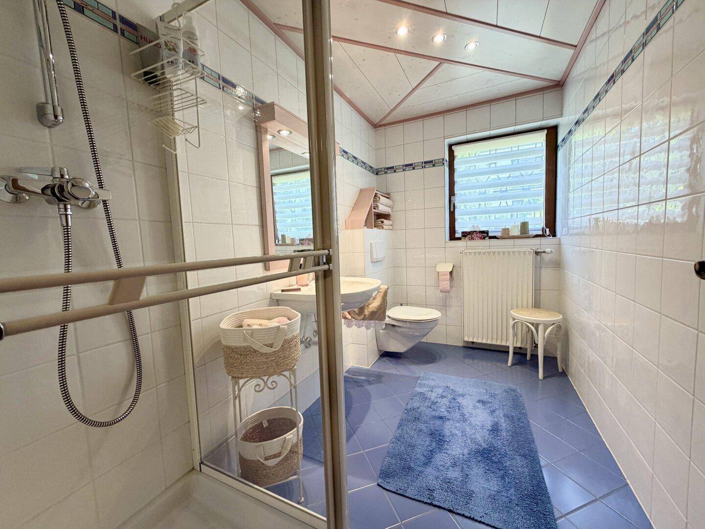Helles Badezimmer mit Dusche, weißen Fliesen und blauen Bodenfliesen.