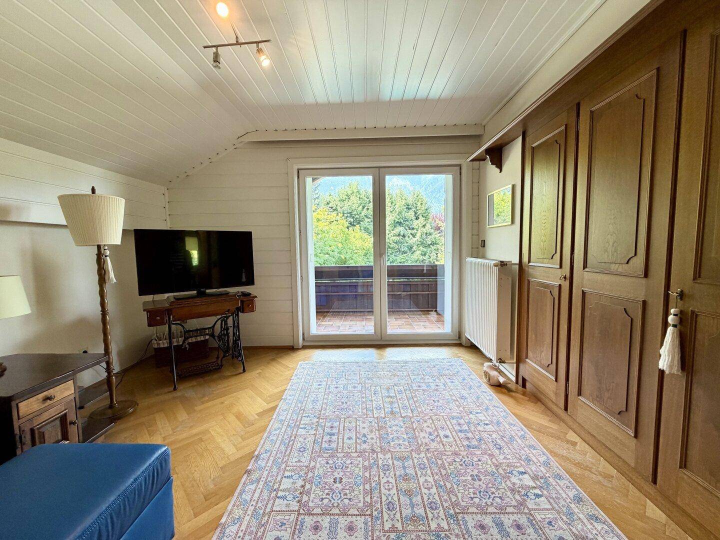 Helles Schlafzimmer im Dachgeschoss mit Holzboden, Einbauschränken und Balkonzugang.