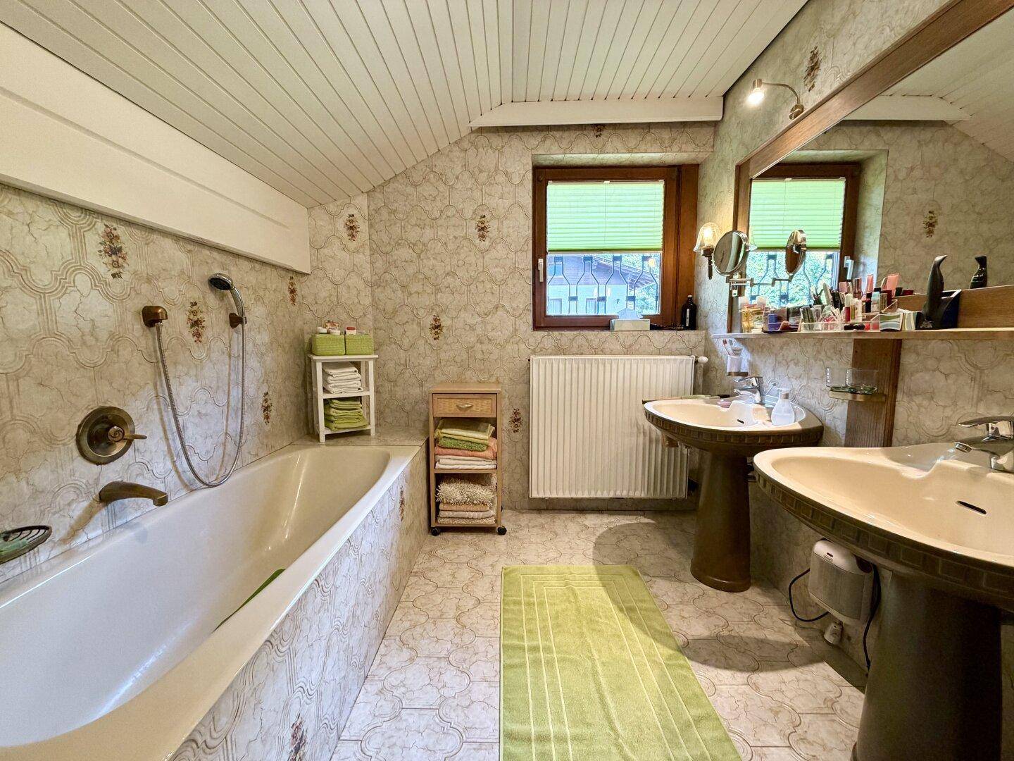 Badezimmer mit Badewanne, zwei Waschbecken und gemusterten Wandfliesen.