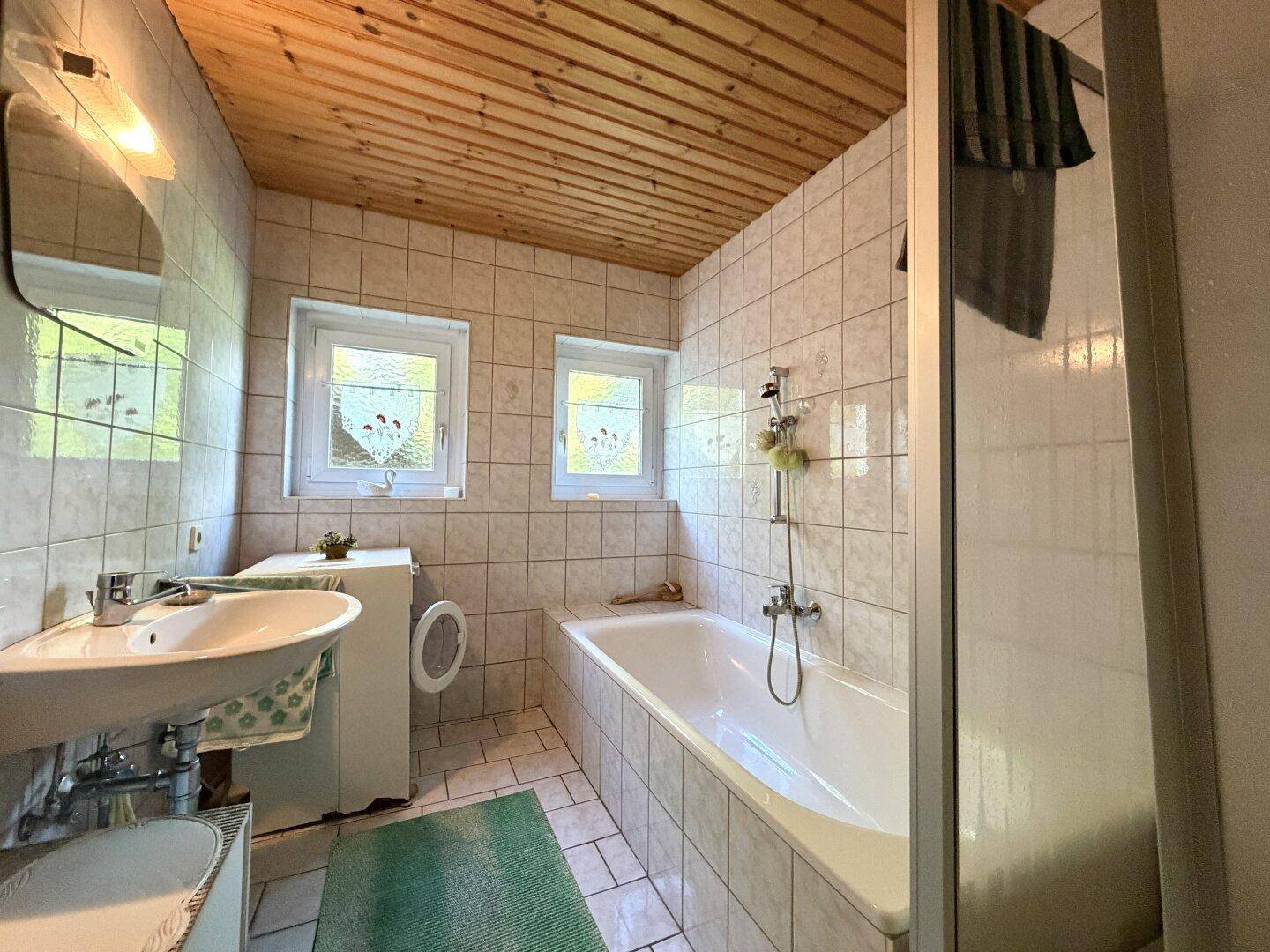 Badezimmer mit Badewanne, Waschbecken, Waschmaschine und Holzdecke.