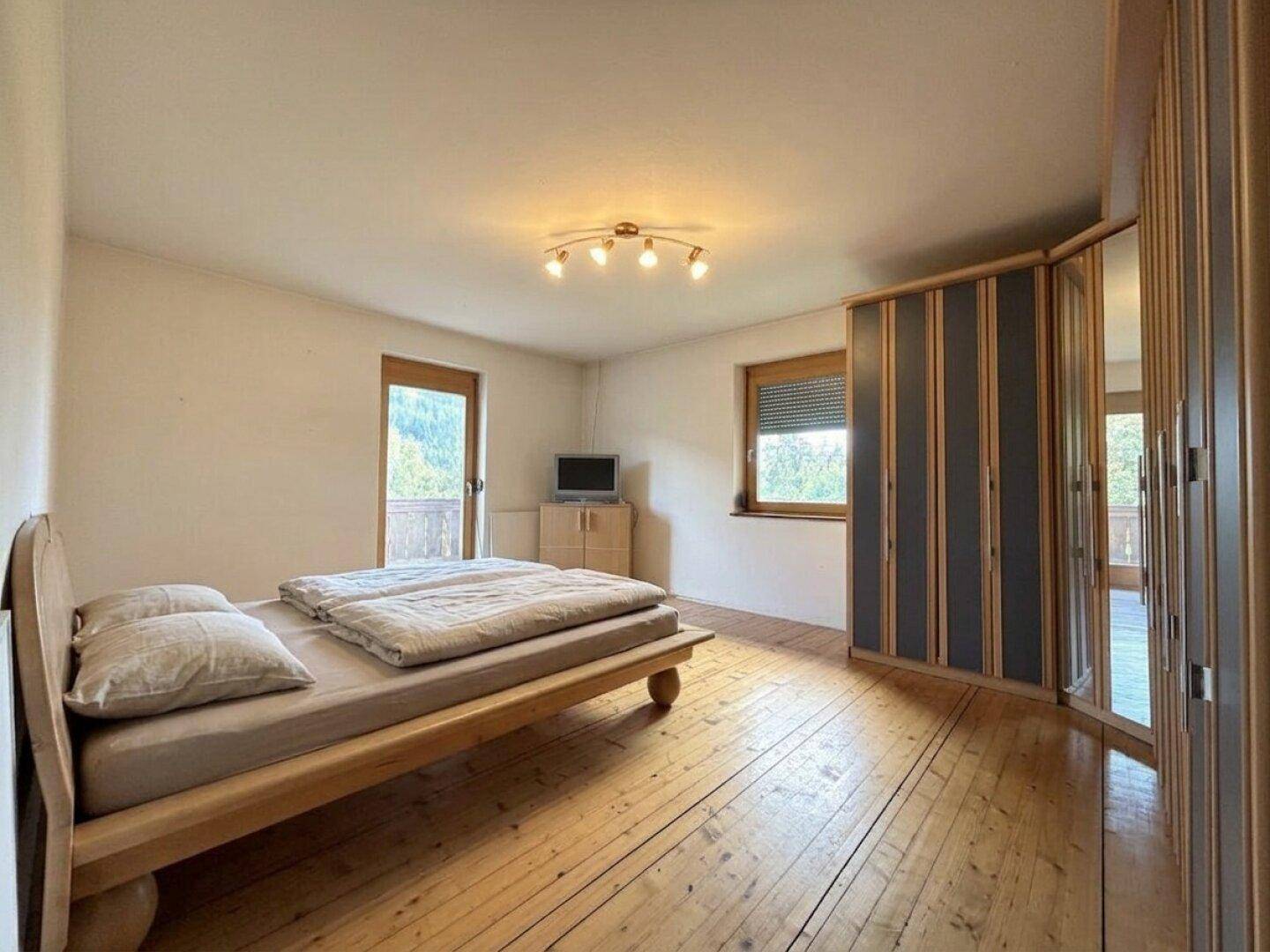 Helles Schlafzimmer mit Holzboden, Doppelbett und großem Spiegelschrank.