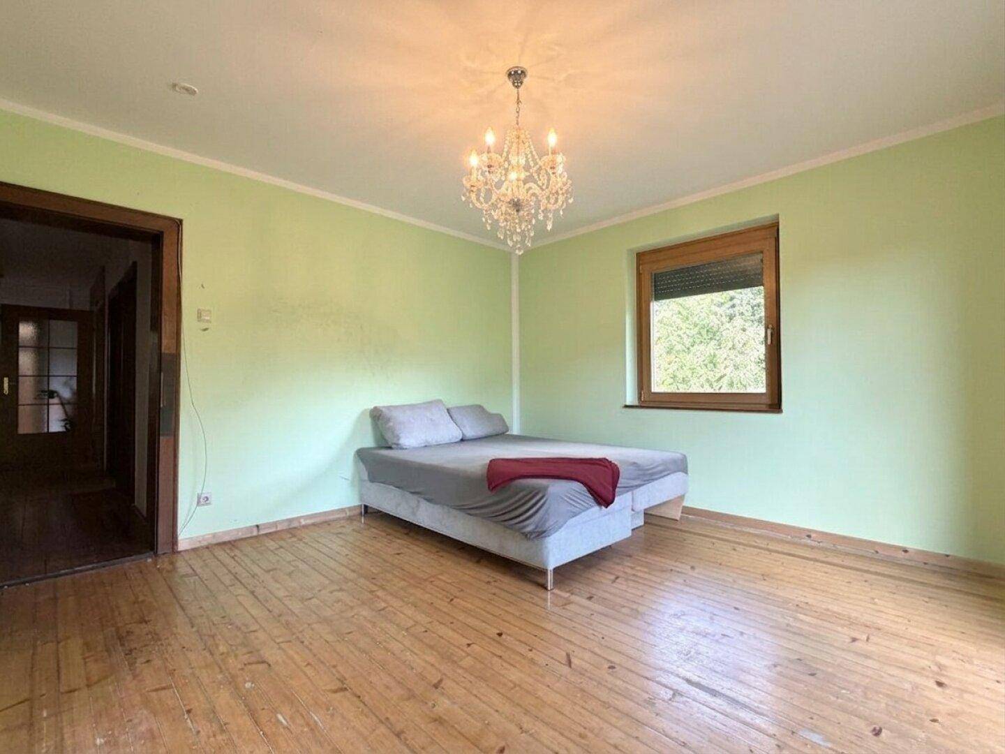Schlafzimmer mit hellgrünen Wänden, Holzboden und einem modernen Kronleuchter.