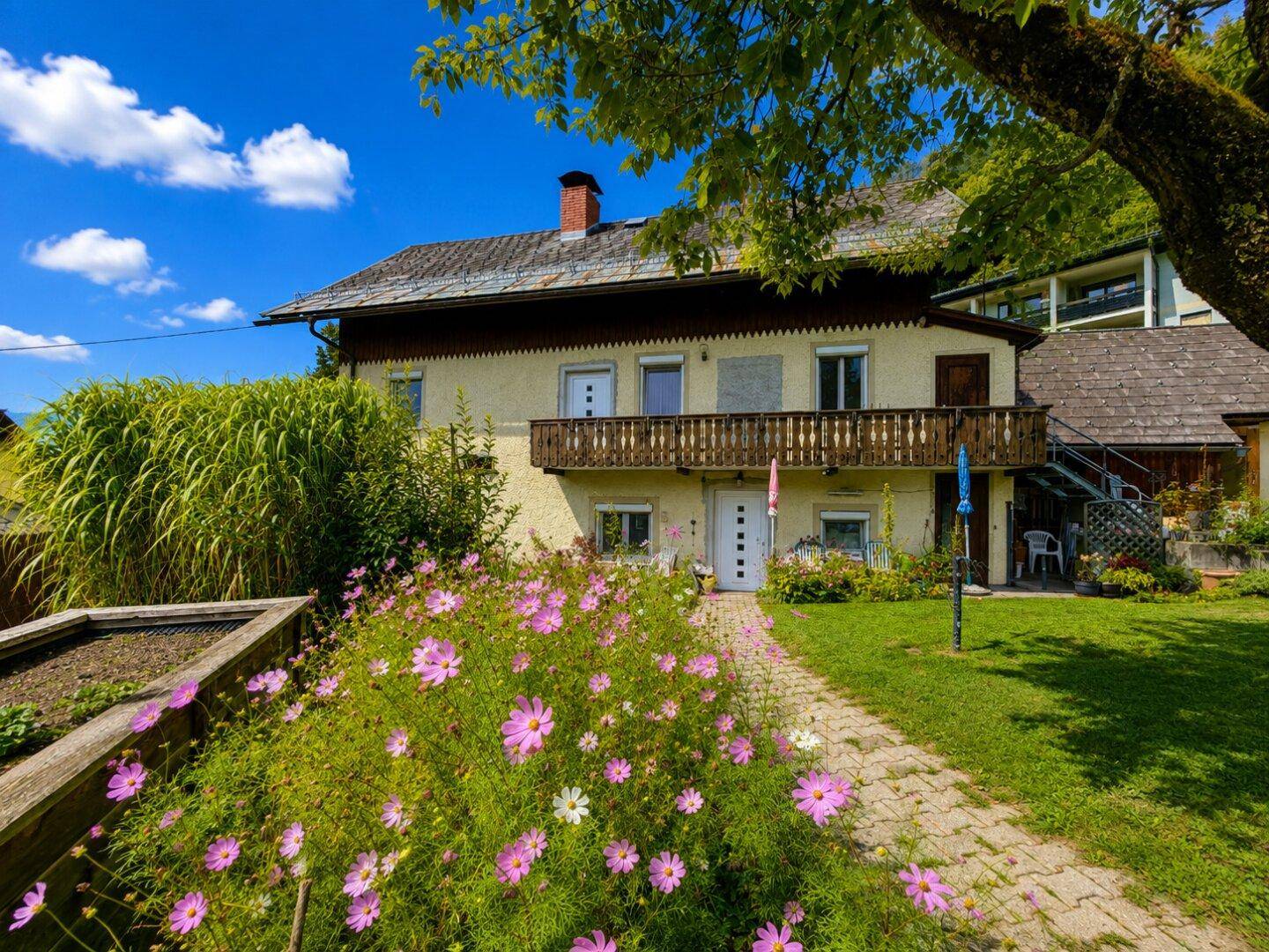 Charmantes Wohnhaus mit blühendem Vorgarten, gepflastertem Weg und traditionellem Balkon.