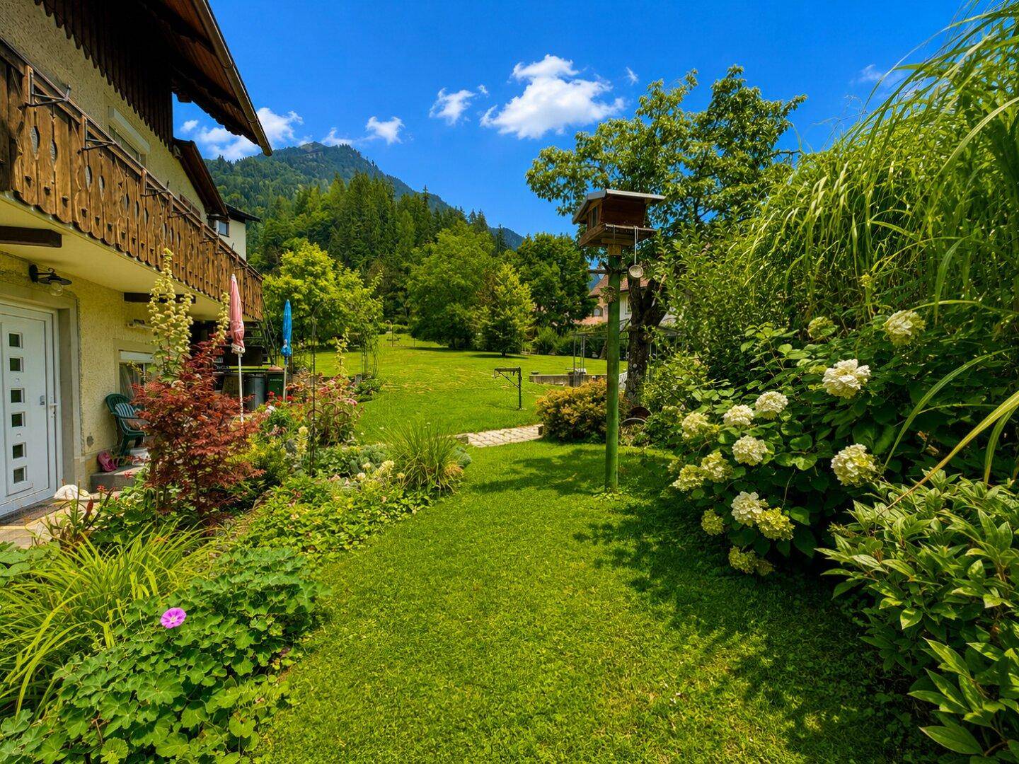 Gepflegter Gartenweg mit üppiger Bepflanzung und Blick auf die grüne Umgebung und Berge.