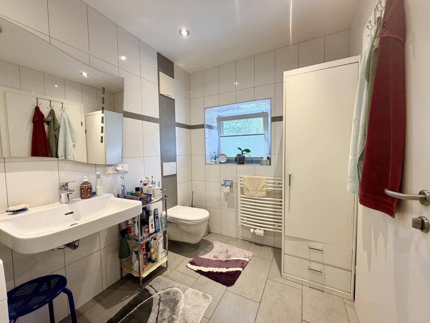 Modern gefliestes Badezimmer mit Dusche, Waschbecken, WC und beheiztem Handtuchhalter.