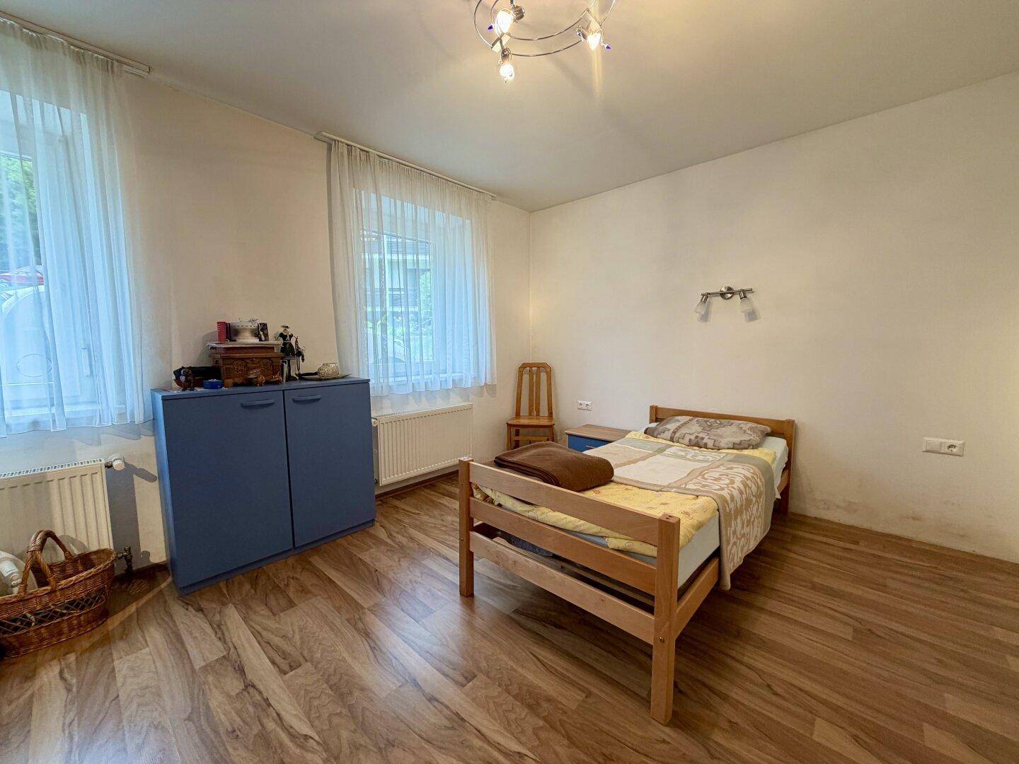 Helles Schlafzimmer mit Holzboden, Einzelbett und zwei Fenstern für viel Tageslicht.
