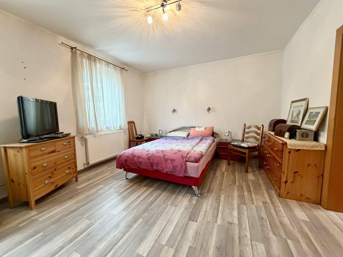 Geräumiges Schlafzimmer mit Doppelbett, Holzmöbeln und hellem Laminatboden.
