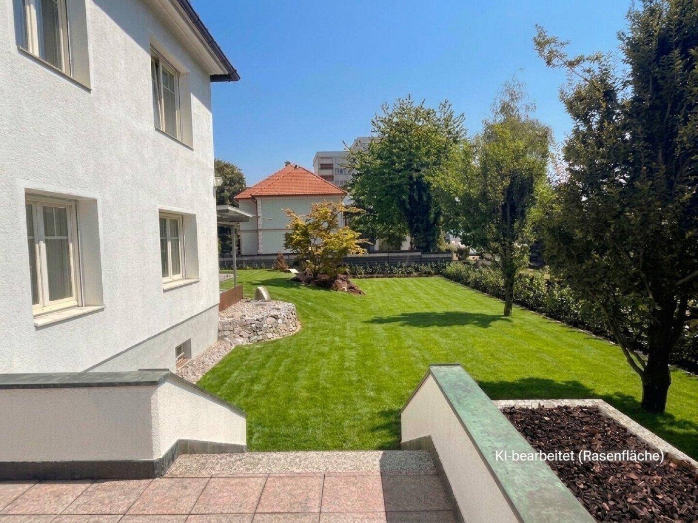 Seitenansicht des Hauses mit weitläufigem Garten, Rasenfläche und einer kleinen Steinterrasse.